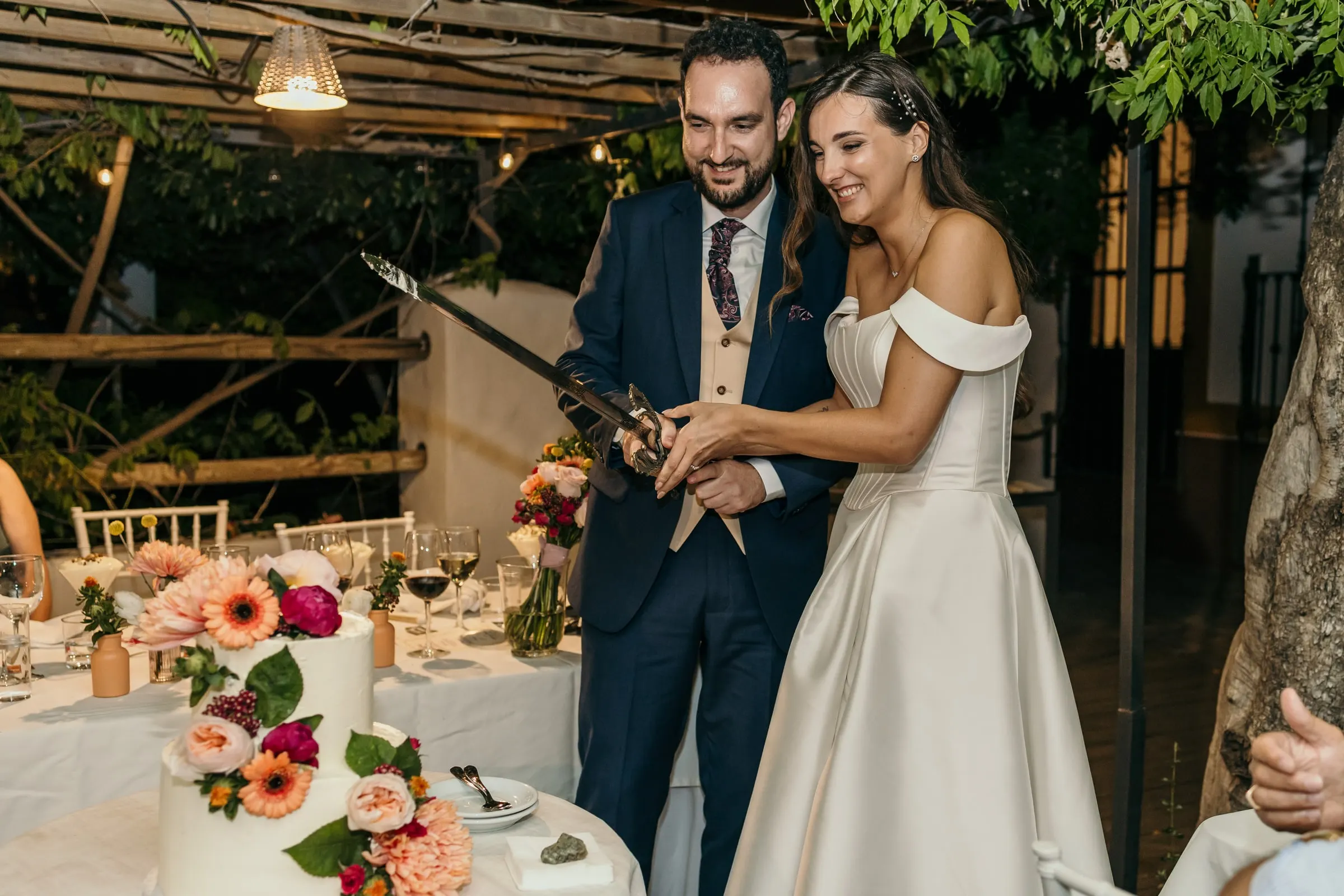 Couple laughing as they slice the wedding cake with a sword at the reception