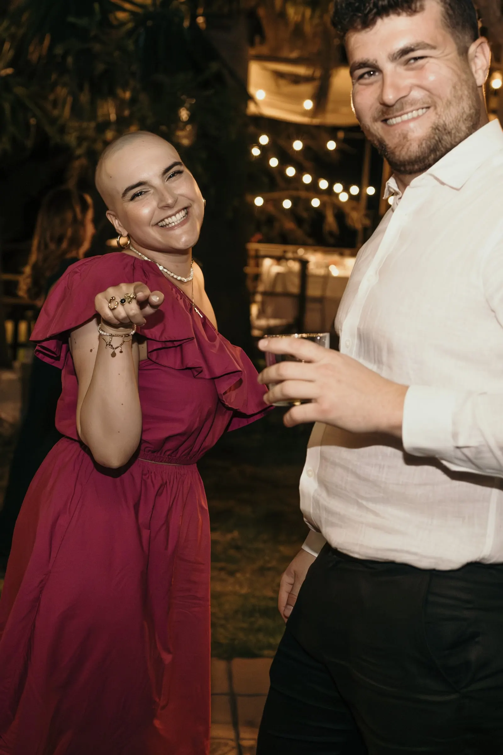 Friend in magenta and a guest in a white shirt posing mid-dance under string lights