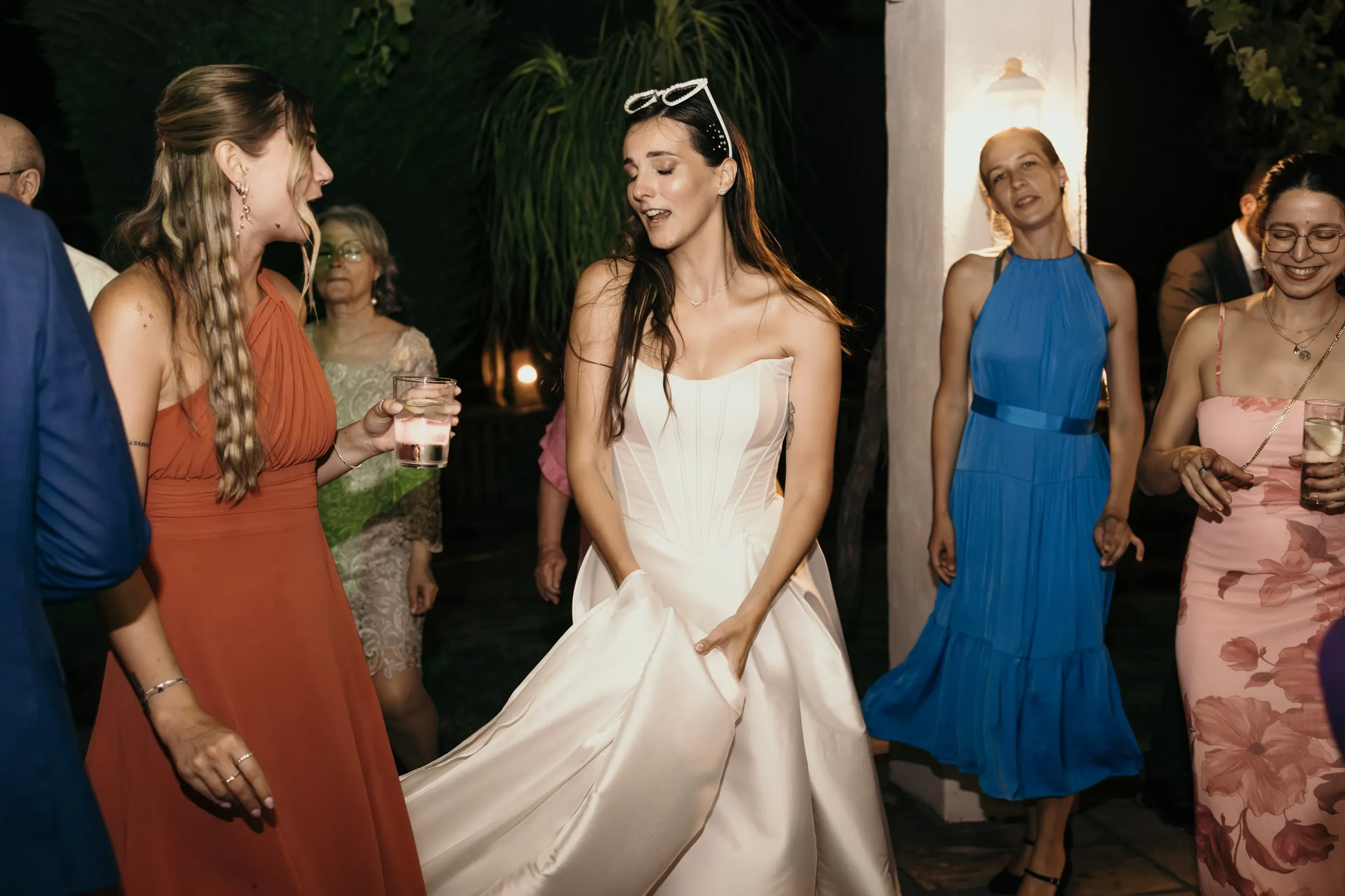 Bride dancing with friends in colourful dresses, sunglasses pushed up on her head