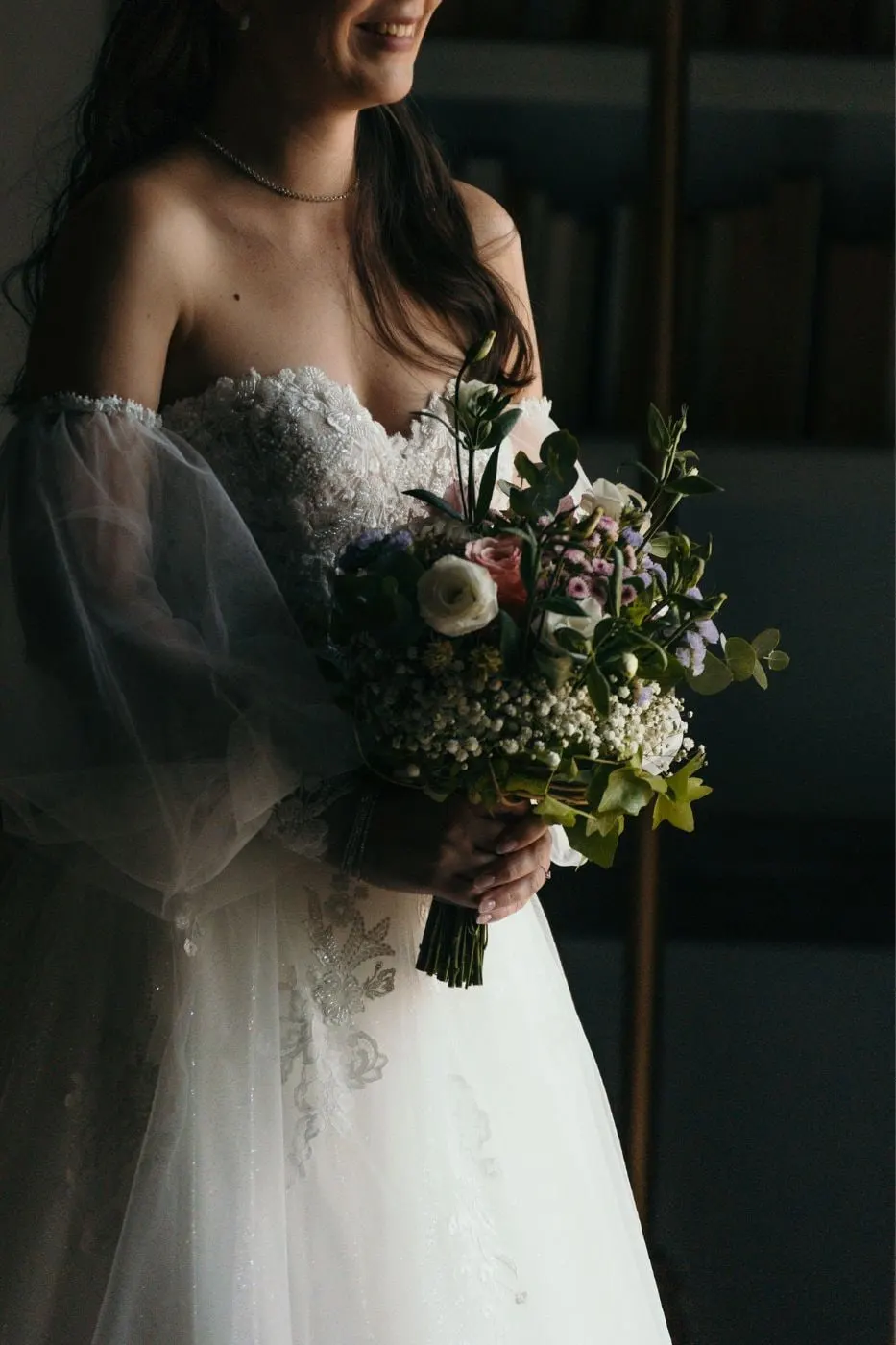 Bride in a sheer-sleeved gown holding a wild flower bouquet in soft window light, Costa del Sol