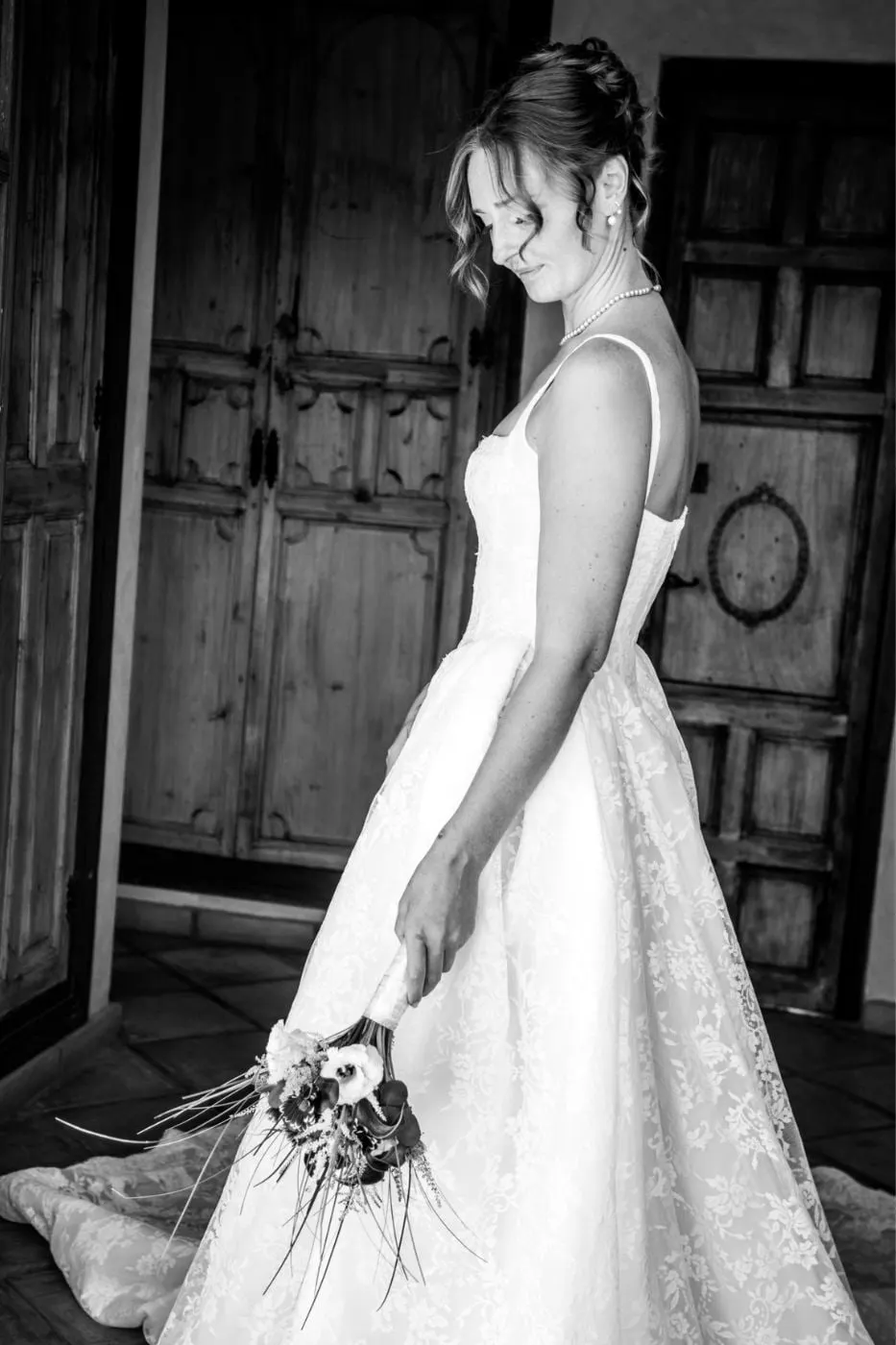 Black and white of the bride in a lace gown looking down at her bouquet by a wooden door, Costa del Sol