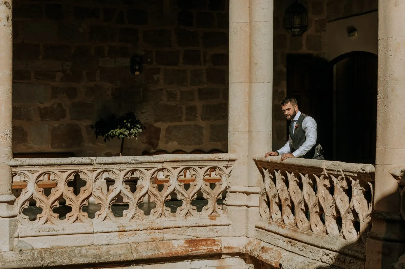 El novio, con chaleco, se apoya en la balaustrada de piedra labrada de un patio antiguo, Costa del Sol