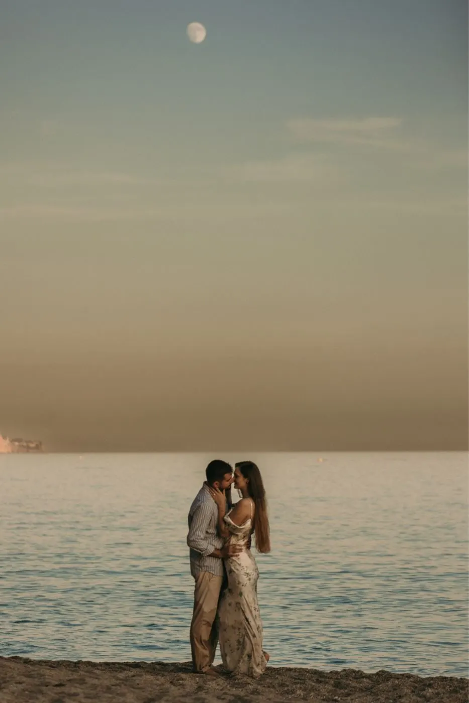 Los novios abrazados en la orilla al atardecer, con la luna sobre el mar, Nerja