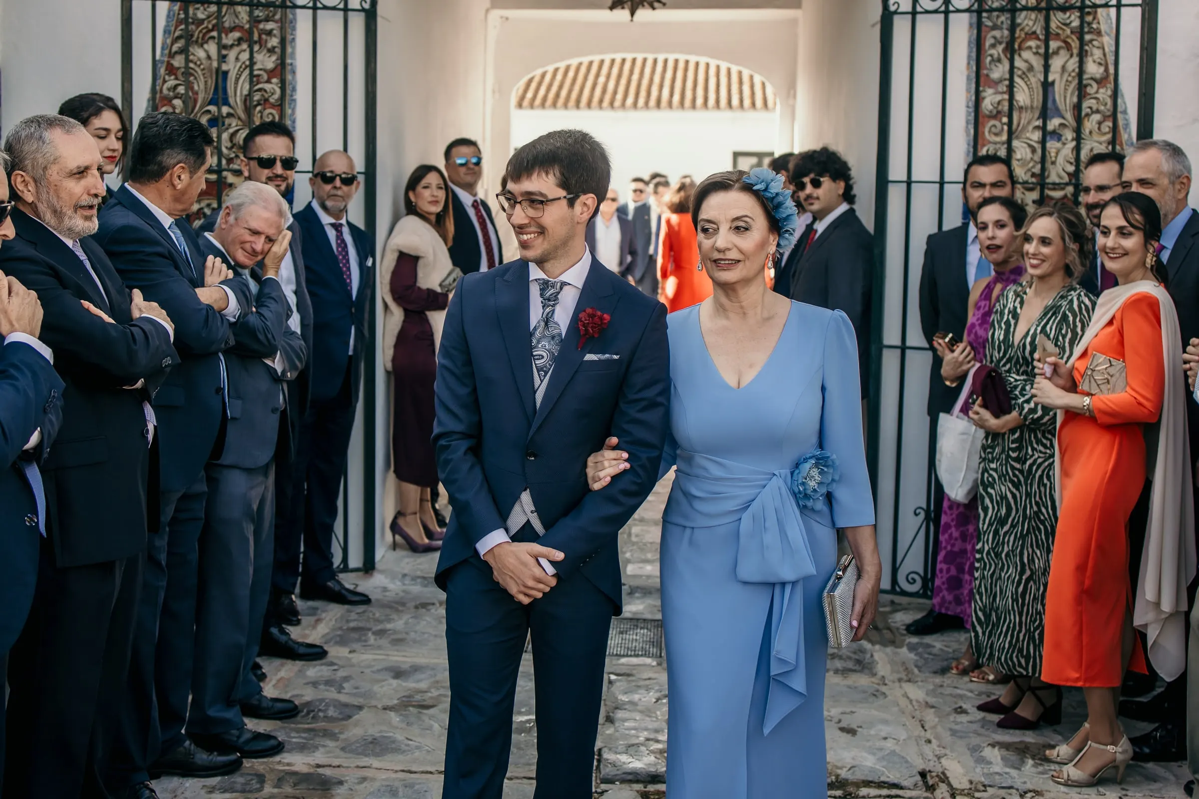 Groom walking into the cortijo courtyard on his mother's arm between rows of guests