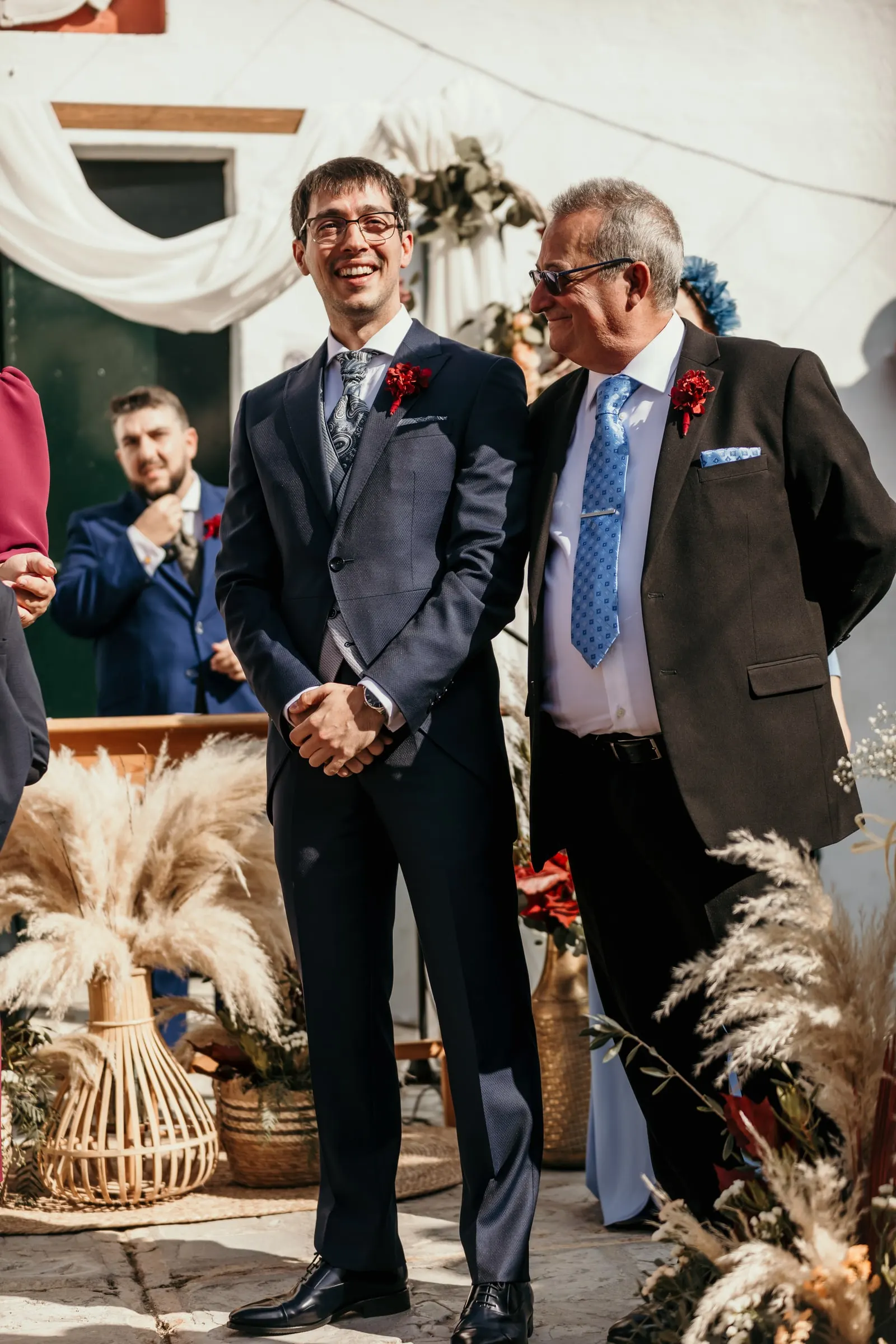 Groom laughing with his father at the ceremony table decorated with pampas grass in the whitewashed courtyard