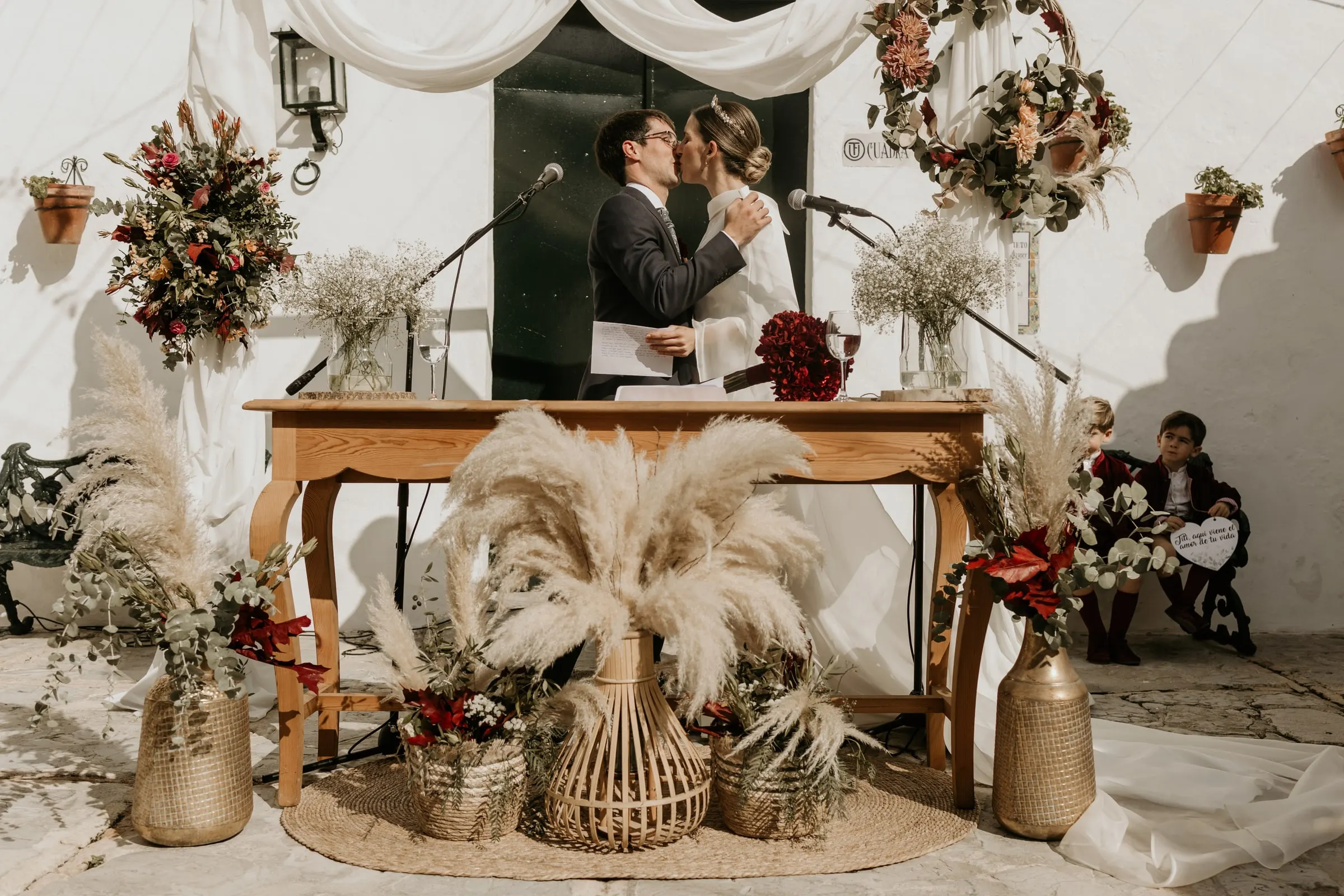 First kiss as a married couple at the courtyard altar of pampas grass and gold vases