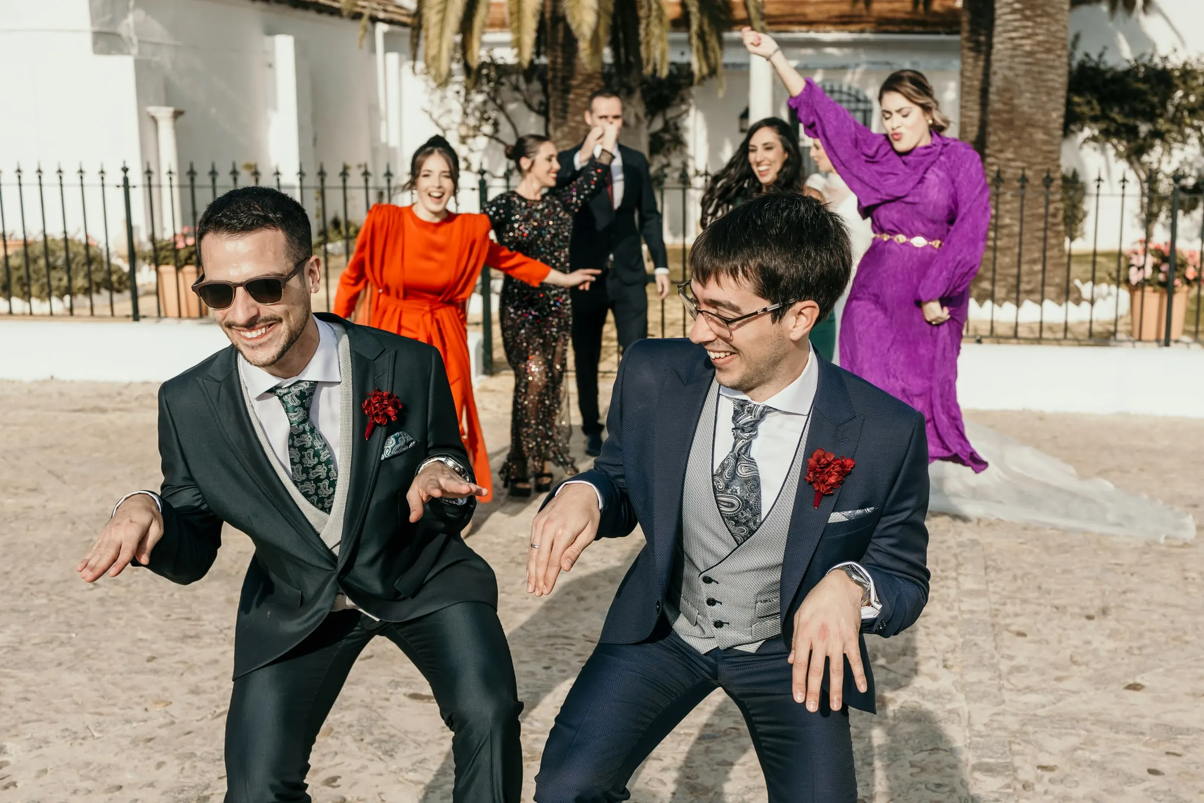Groom and his friend dancing in sunglasses in the cortijo yard with guests behind them