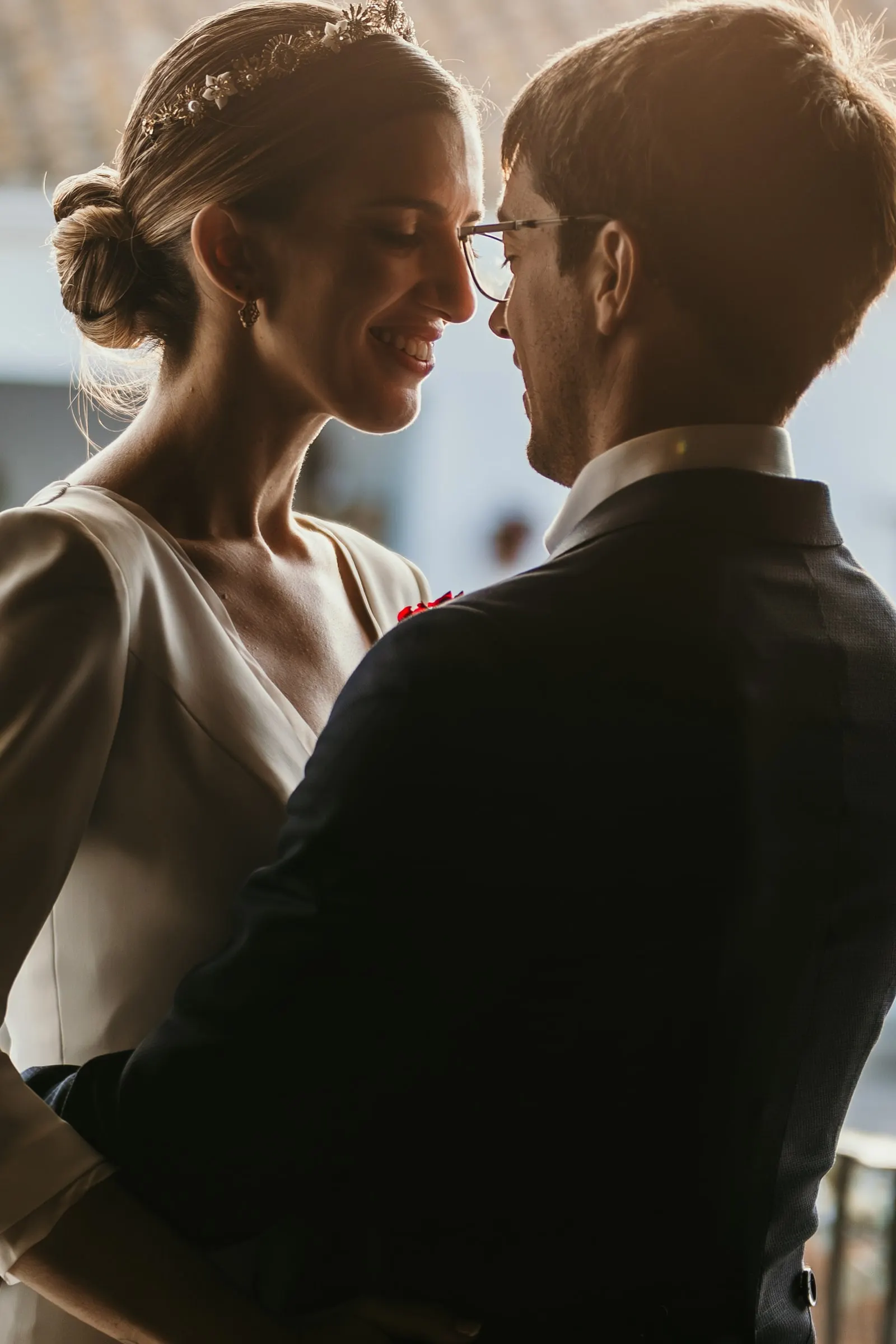 Backlit close-up of the bride and groom smiling face to face in the late afternoon
