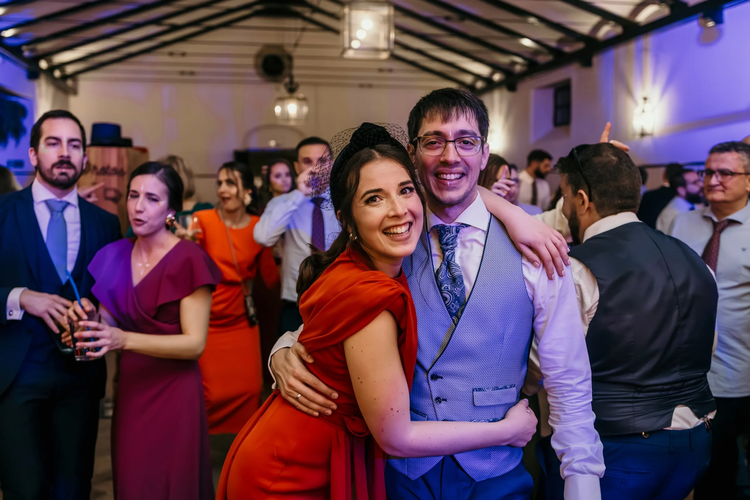 Guest in red hugging the groom among dancers under the beamed ceiling of the cortijo hall