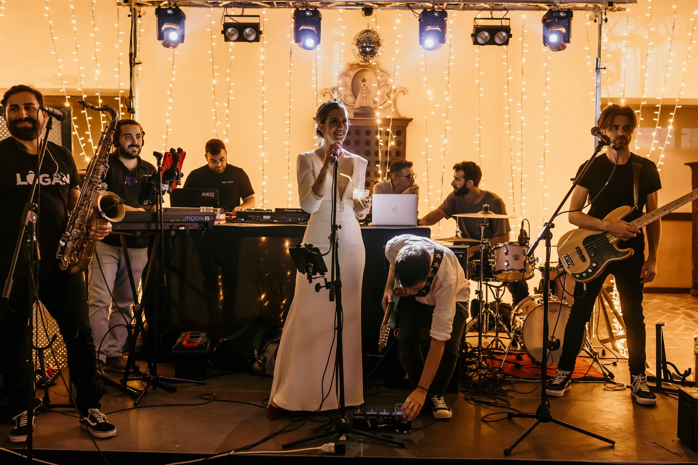 Live band playing on a stage of lights and fairy-light curtains as the bride sings along