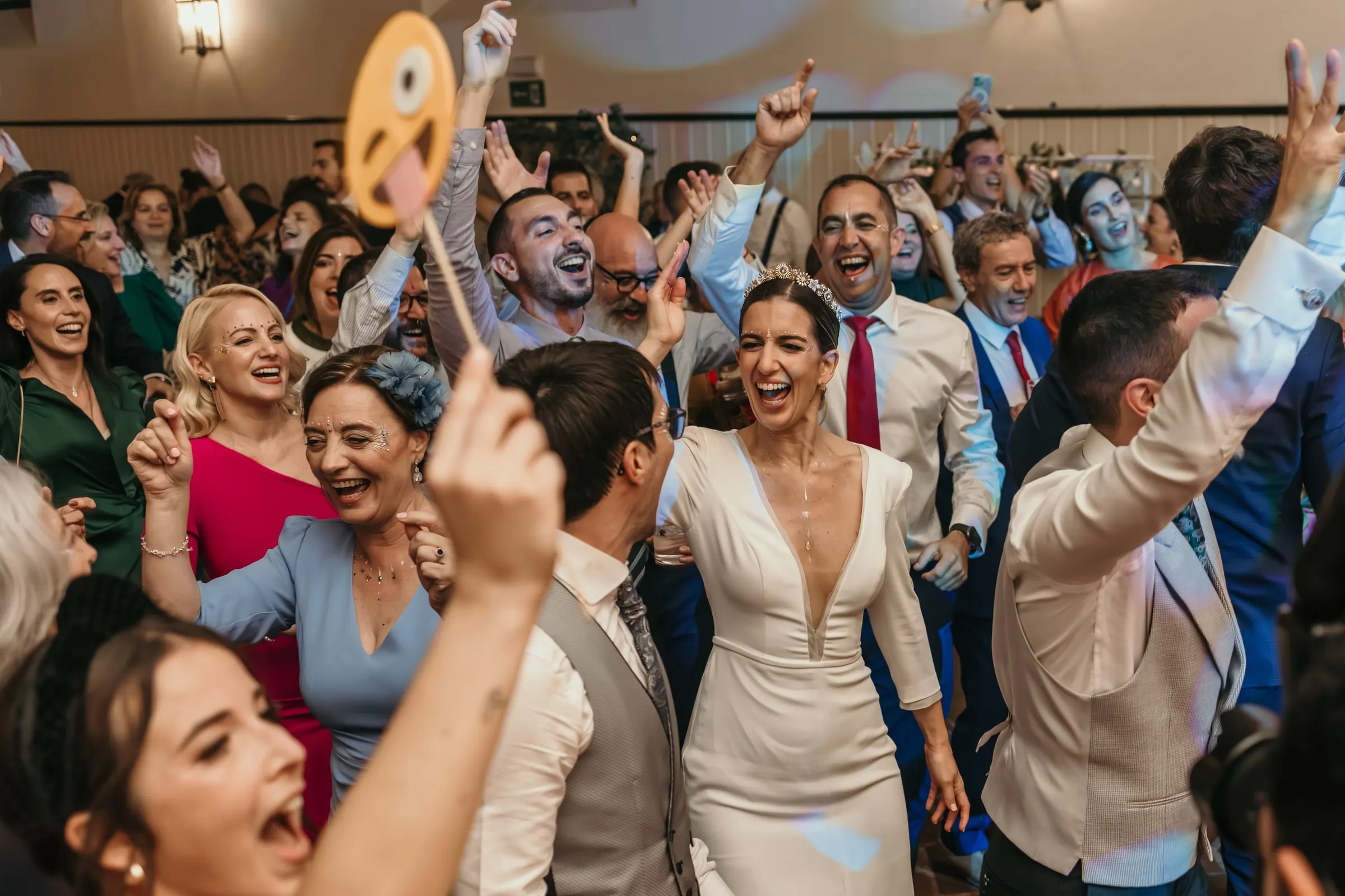 Bride dancing among cheering guests holding up a smiling emoji sign