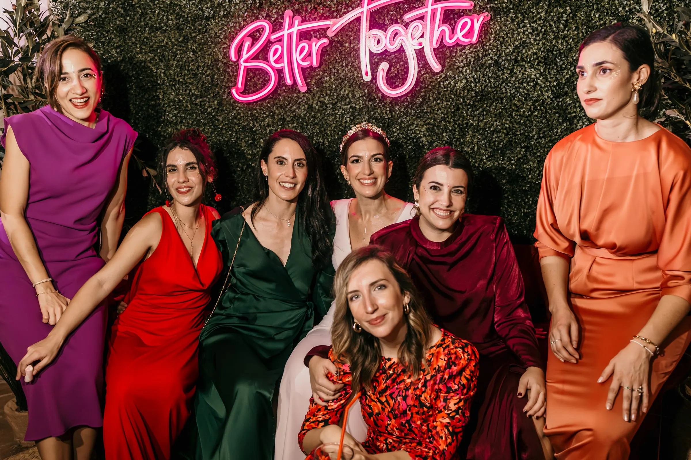 Bride's friends posing in jewel-coloured dresses under the 'Better Together' neon sign