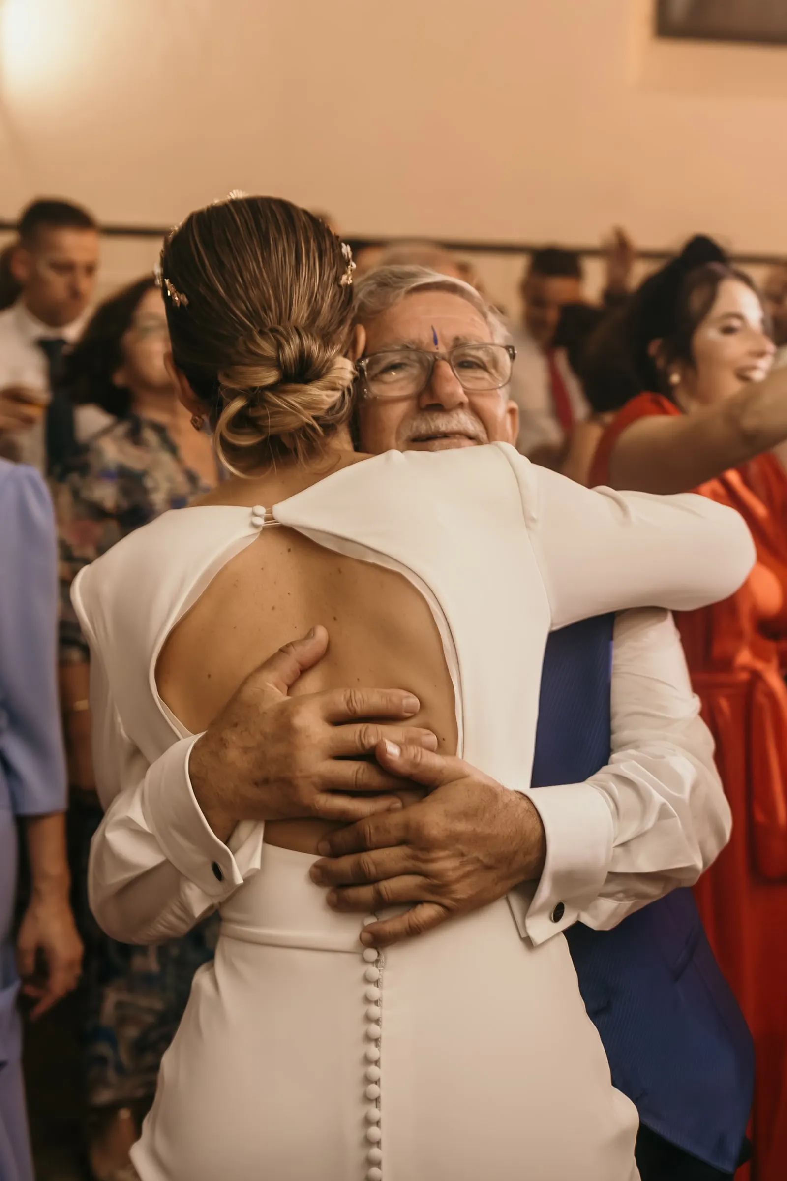 Older guest hugging the bride on the dance floor, her open-back dress with covered buttons