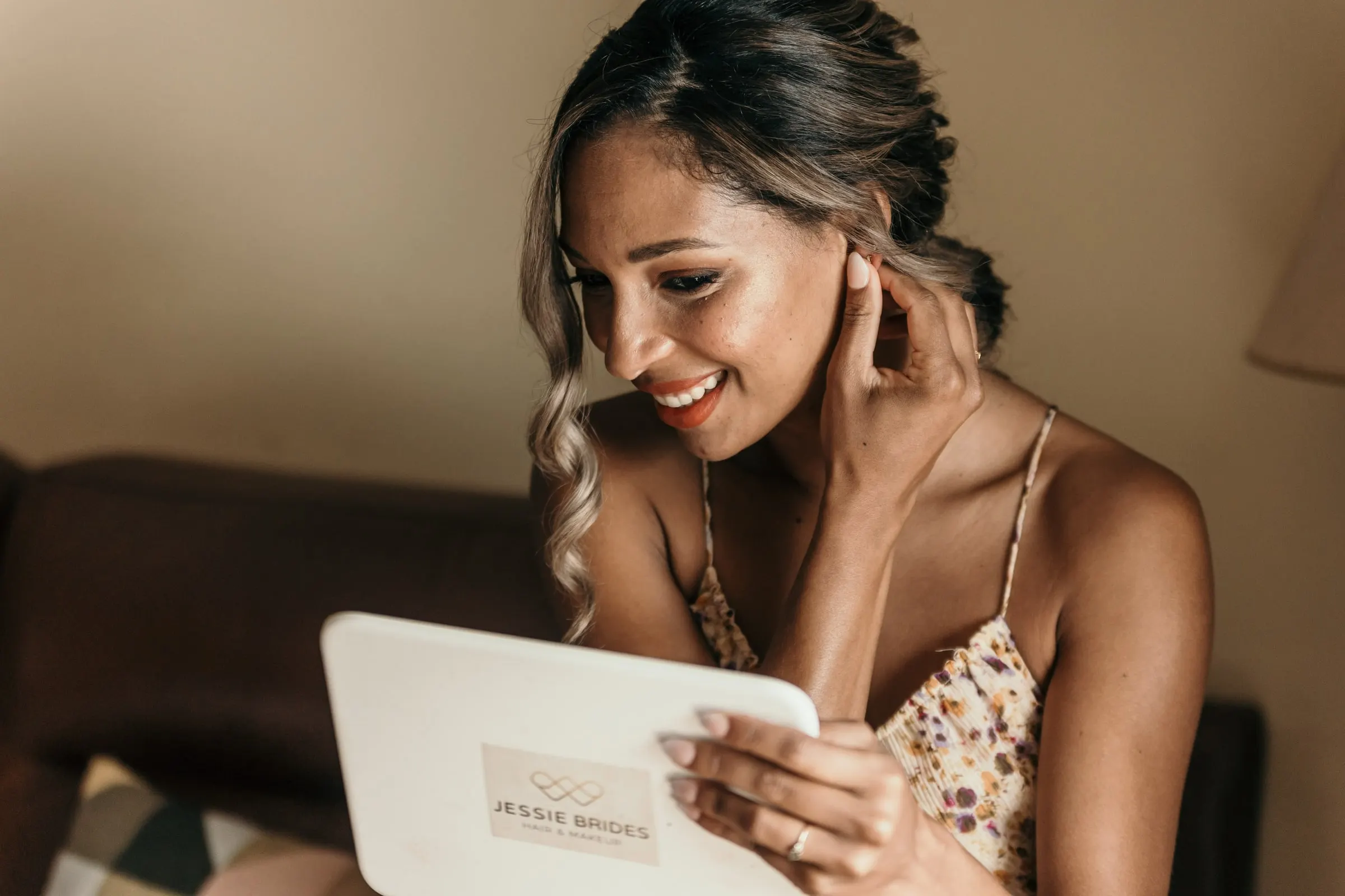 La novia se toca el pendiente y sonríe al espejo tras la peluquería y el maquillaje, la mañana de la boda