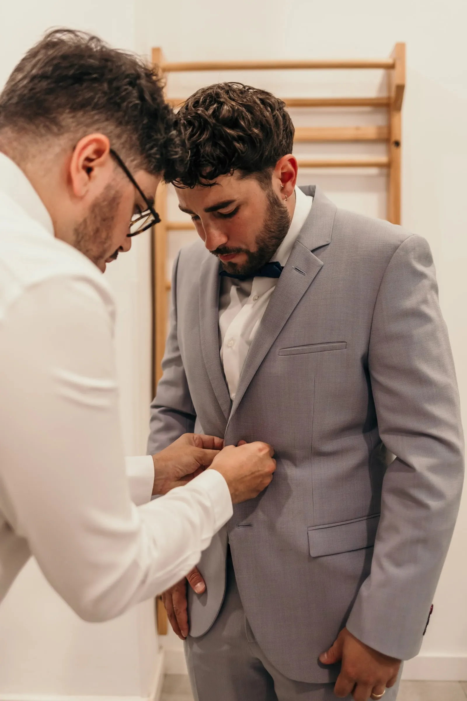 Un amigo abrocha la chaqueta gris claro del novio, casi frente con frente