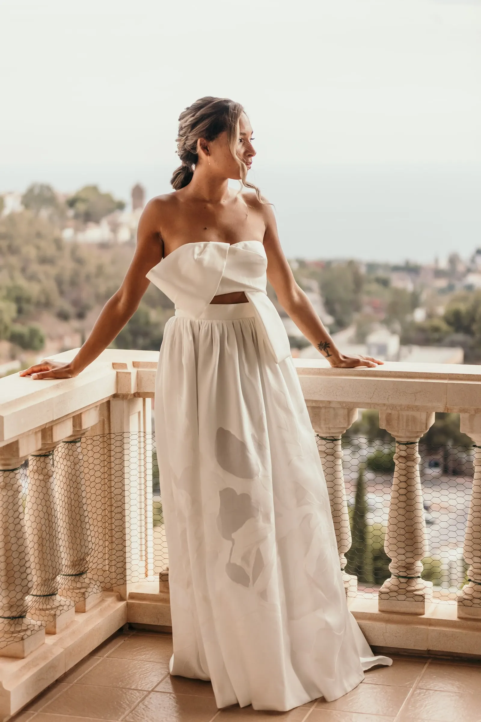 La novia, con vestido palabra de honor y gran lazo delantero, apoyada en la balaustrada blanca de la villa