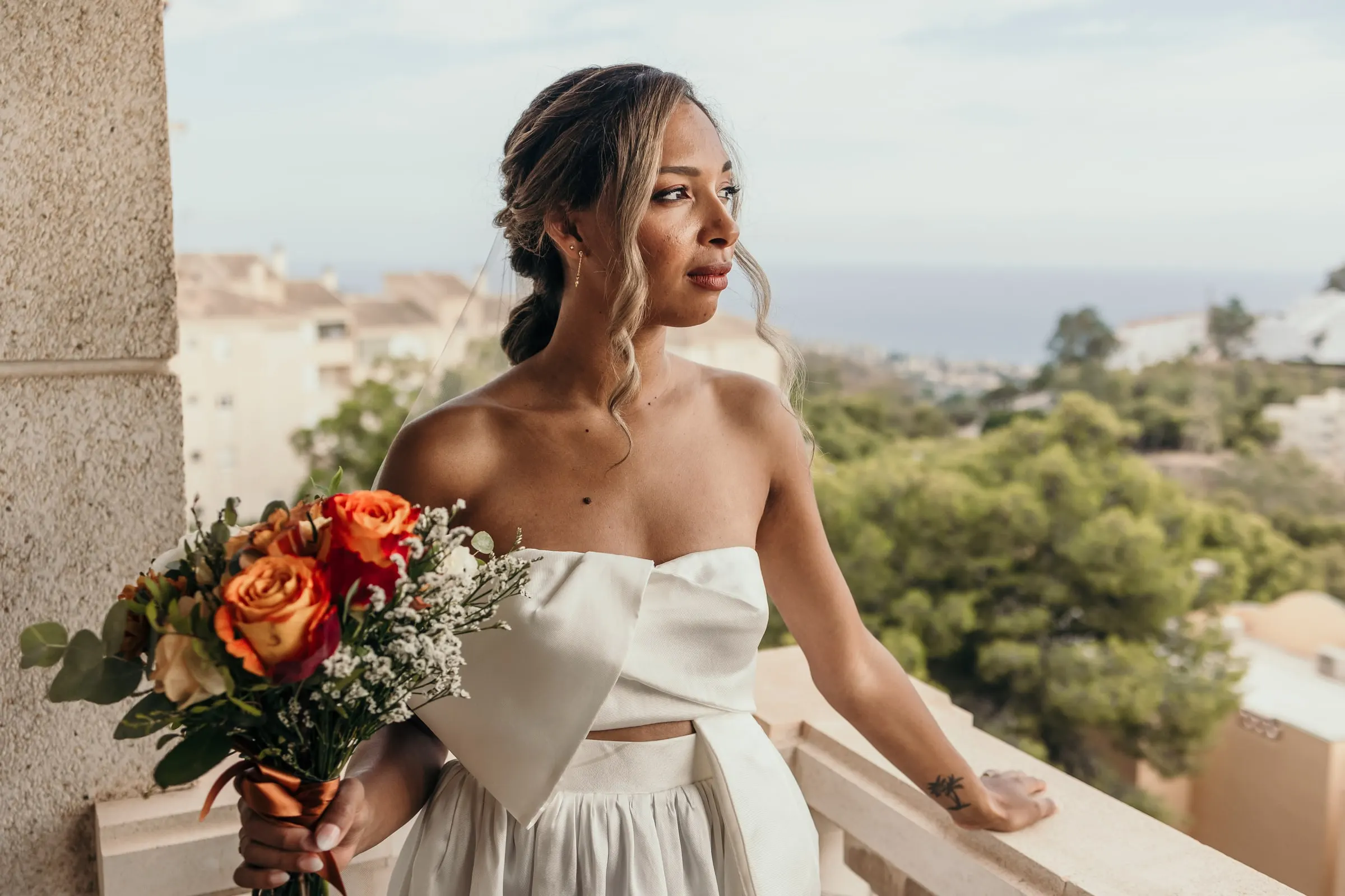 La novia con su ramo de rosas naranjas en un balcón con el Mediterráneo en el horizonte