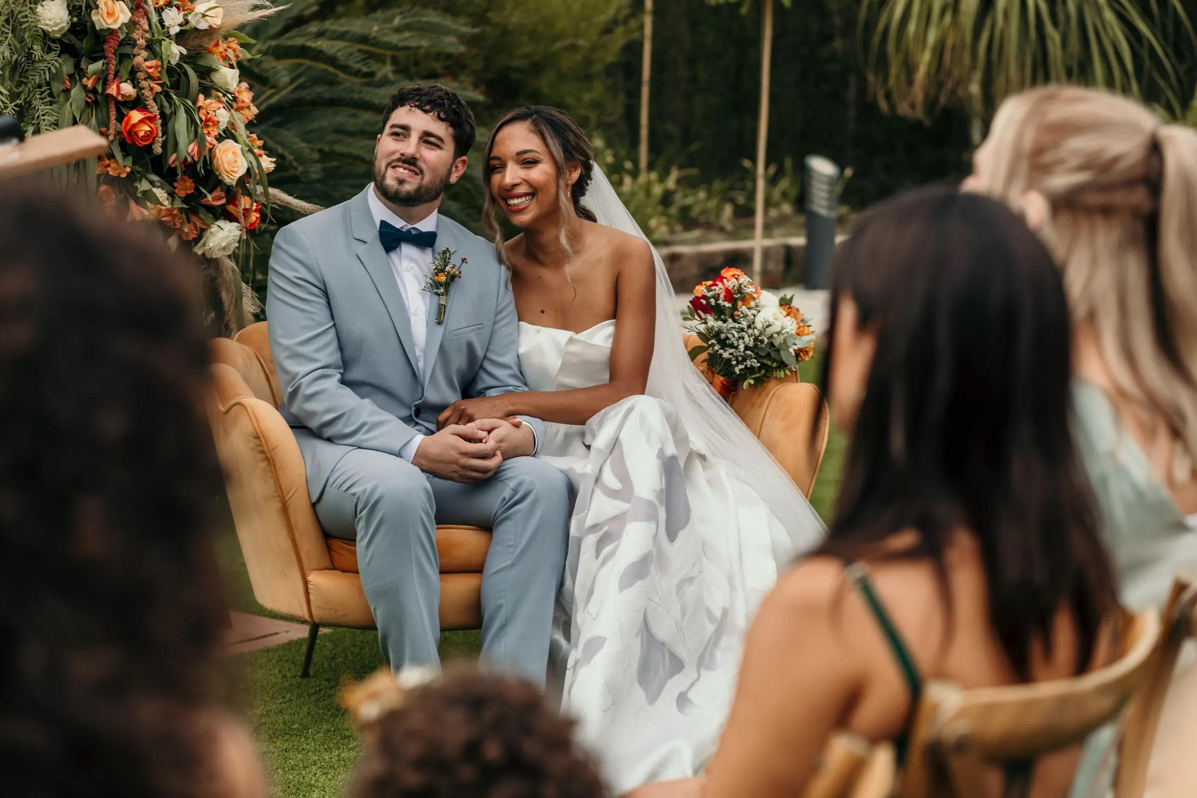 Los novios sentados en la ceremonia, vistos entre dos invitadas de la primera fila