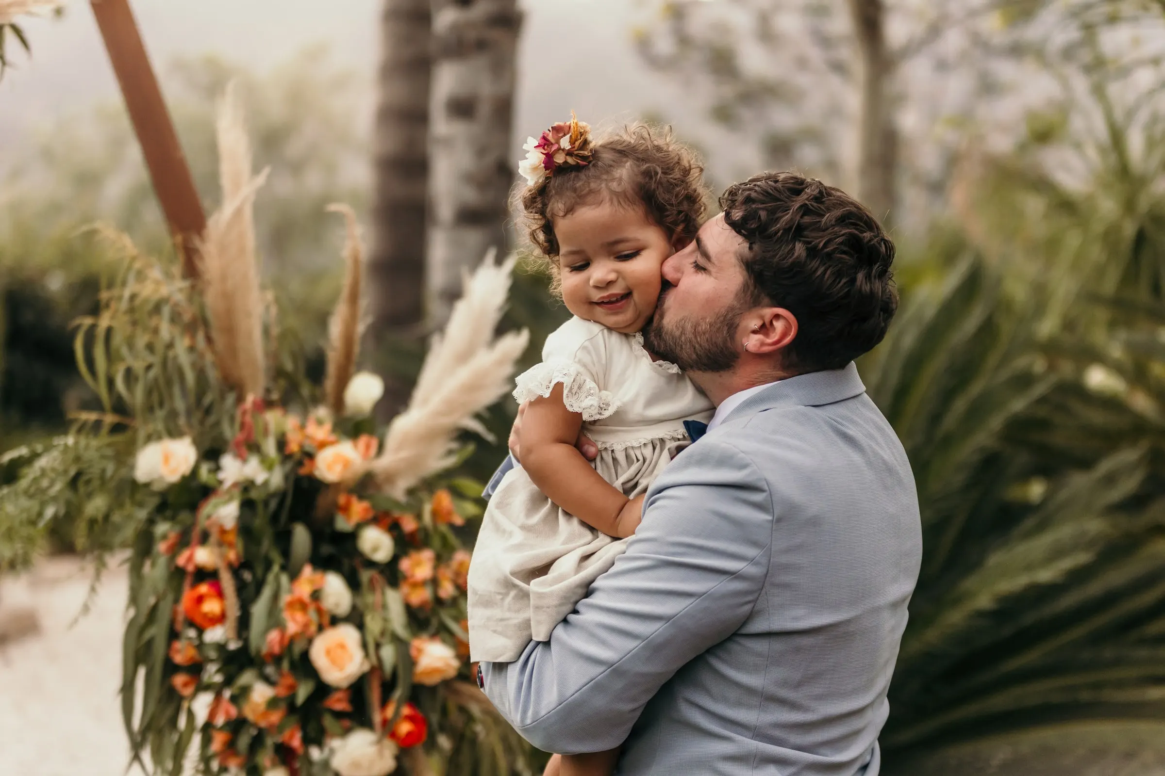 El novio besa en la mejilla a la niña junto al arreglo de pampa y rosas