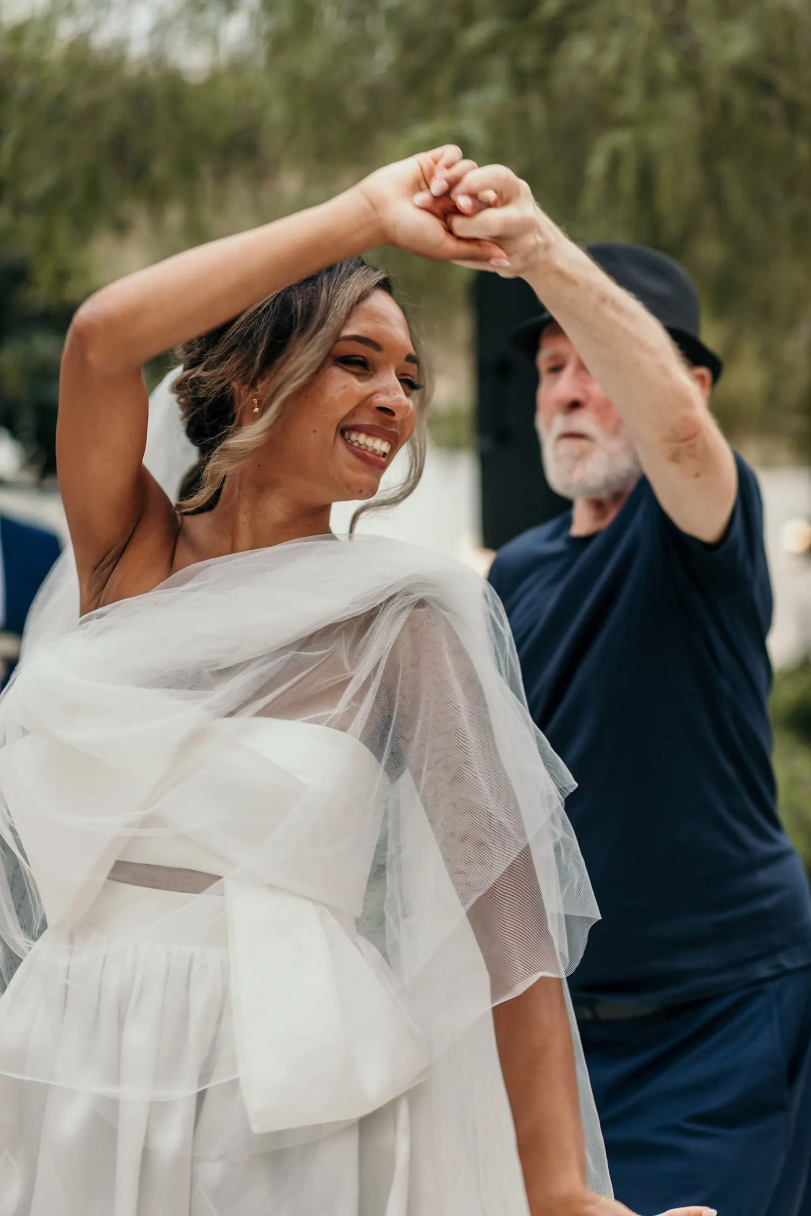 La novia, con un chal de tul, gira bailando con el hombre del sombrero negro
