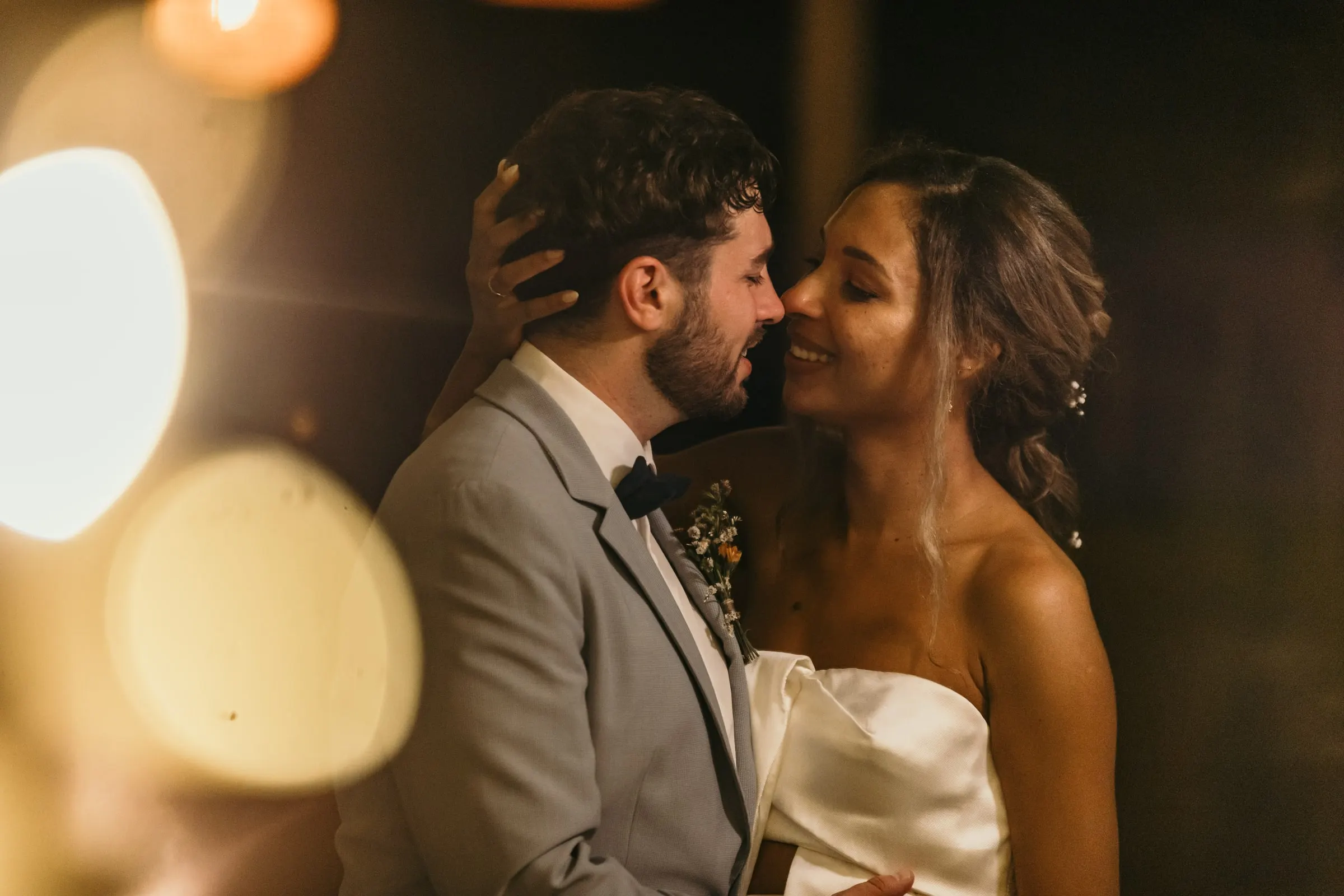 Los novios a punto de besarse, con luces cálidas desenfocadas en primer plano