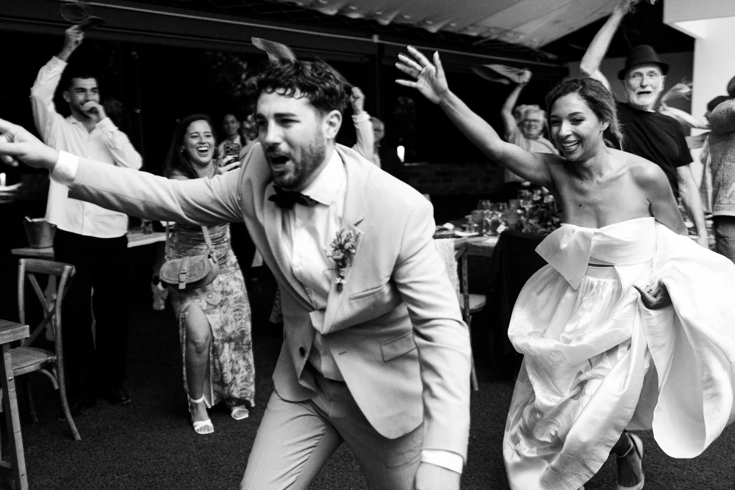 Foto en blanco y negro de los novios bailando a lo loco con sus invitados