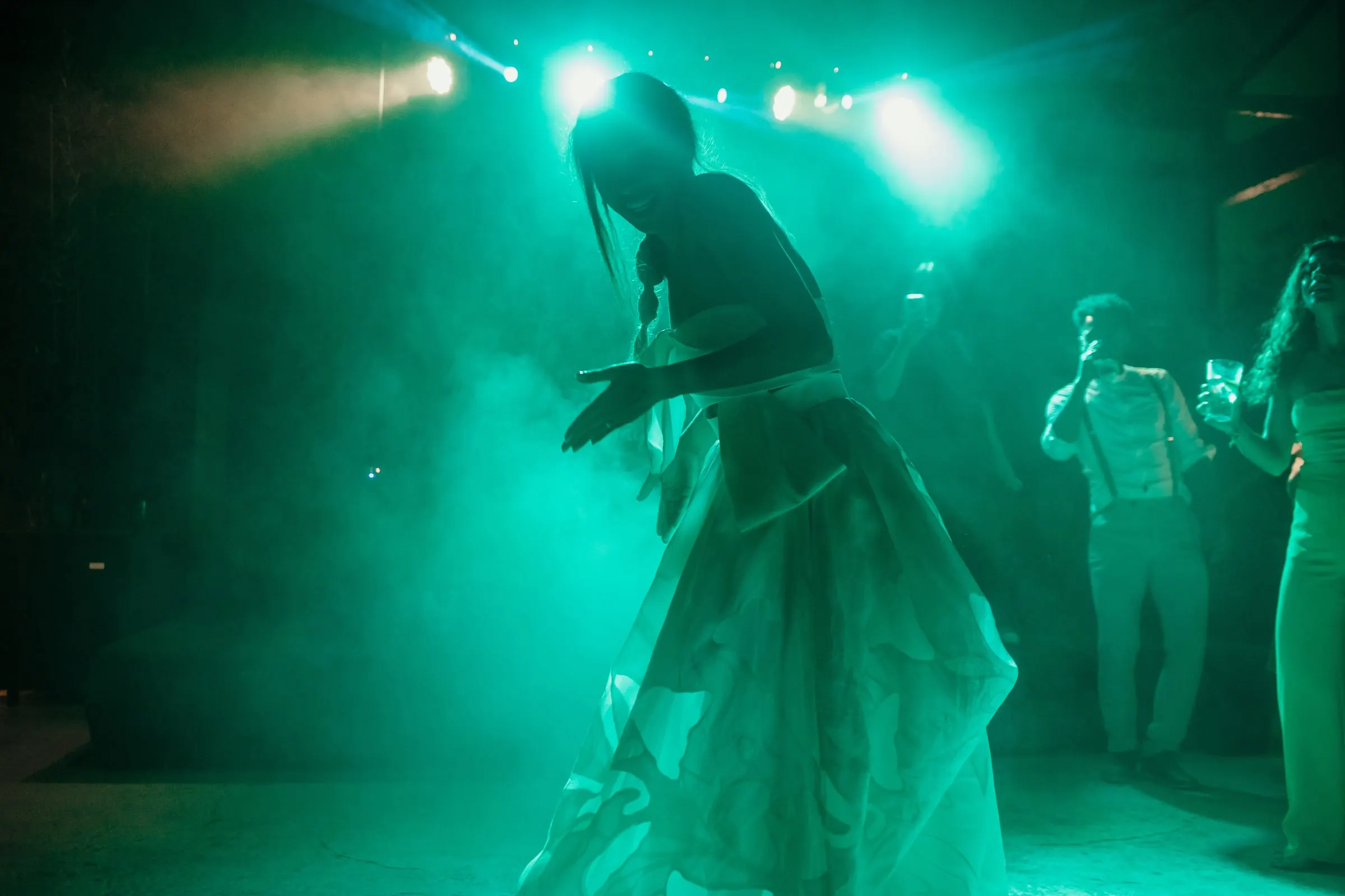 Silueta de la novia bailando entre humo turquesa y focos