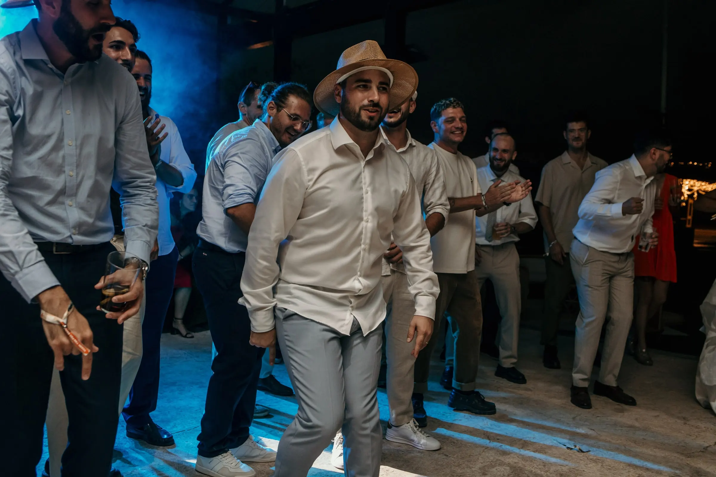 Los amigos del novio, con camisa blanca y sombrero de paja, bailan bajo luz azul