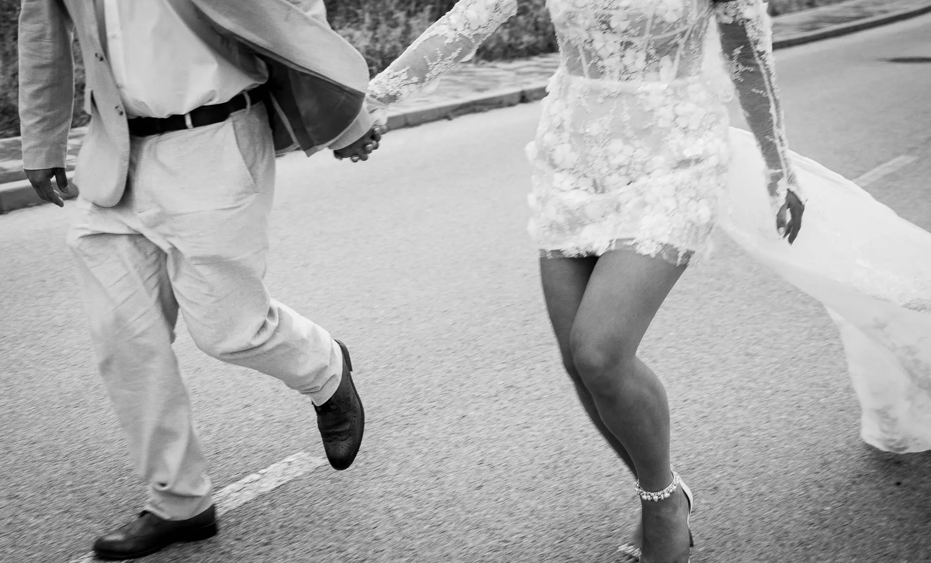 Detalle en blanco y negro de las piernas de los novios caminando de la mano por la carretera, Hacienda San José, Mijas