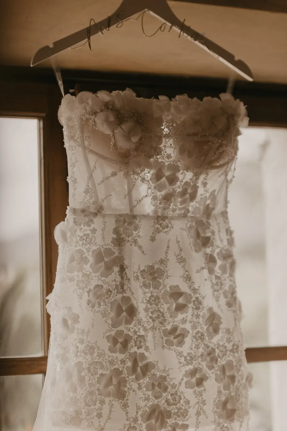Floral lace wedding dress hanging from a personalised hanger by the window, Hacienda San José, Mijas