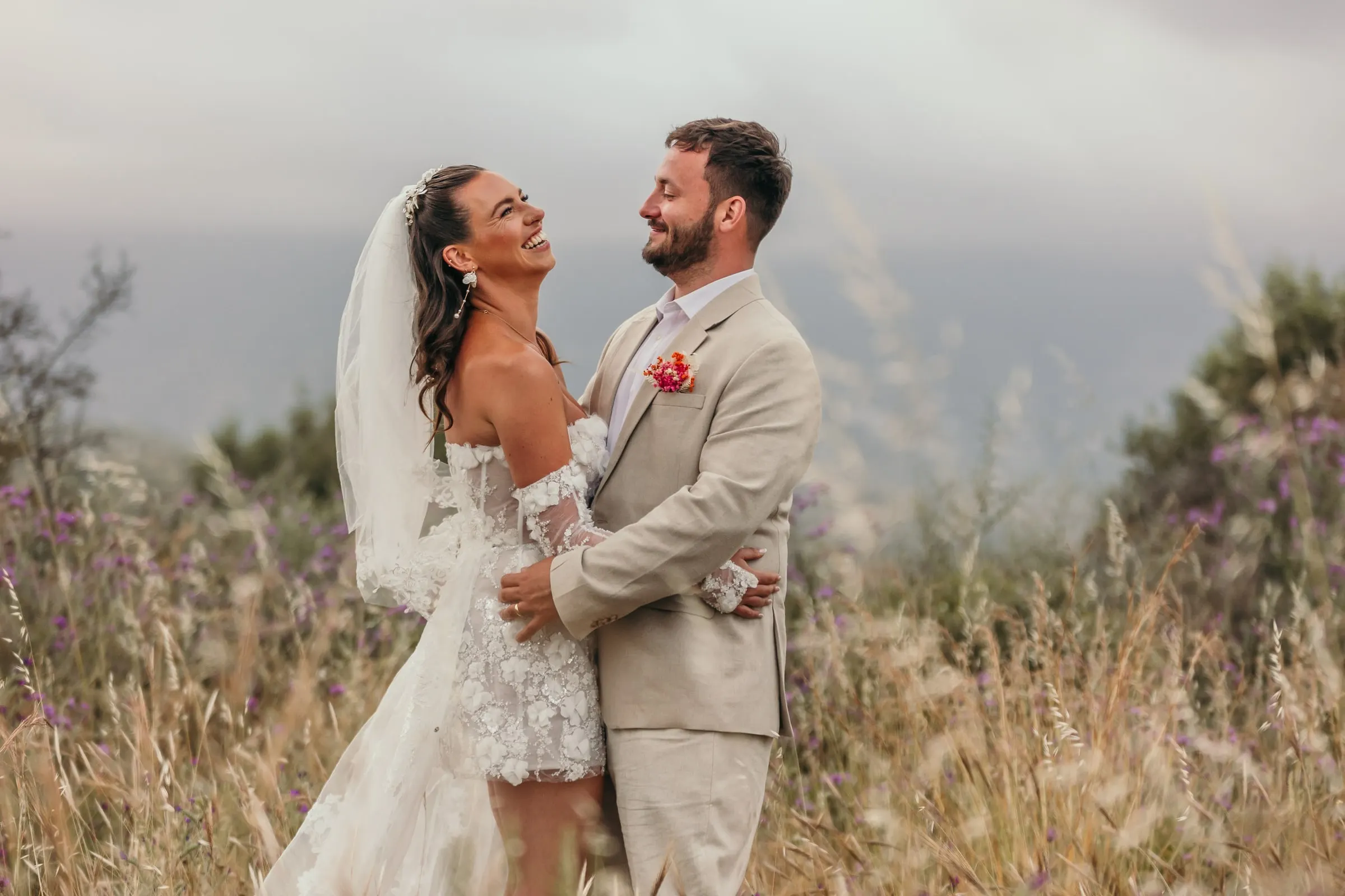 Bride and groom laughing in a meadow of wild grasses above the coast at Hacienda San José, Mijas