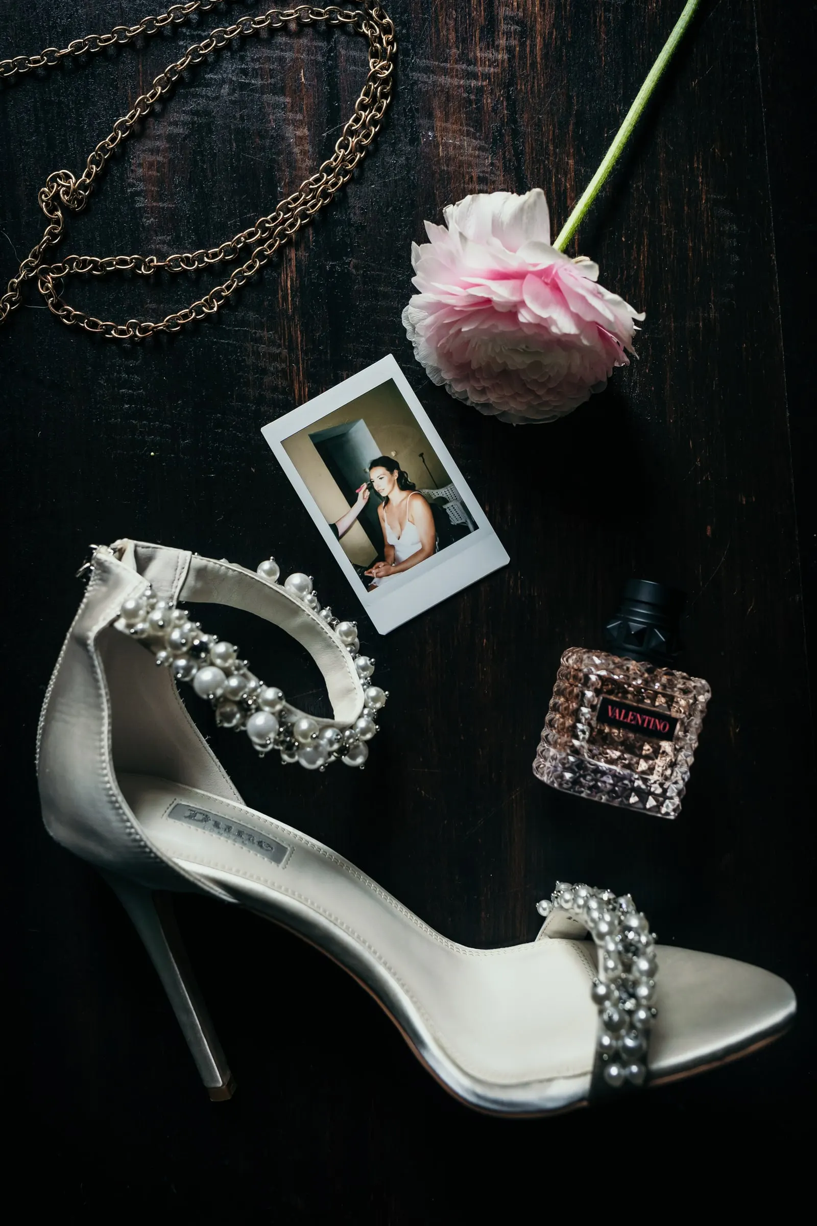 Bridal details on dark wood: pearl sandals, a pink ranunculus, perfume and a Polaroid, Hacienda San José, Mijas