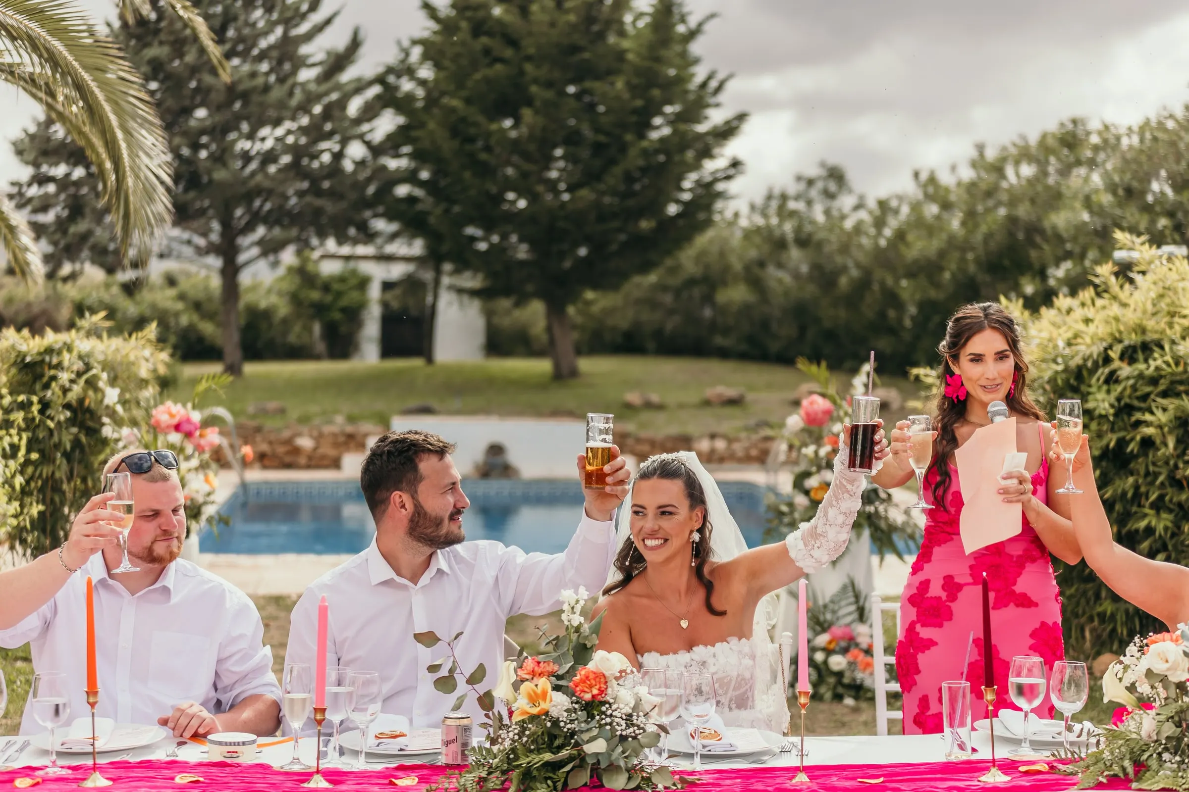 Bride, groom and guests raise their glasses at the top table beside the pool, Hacienda San José, Mijas