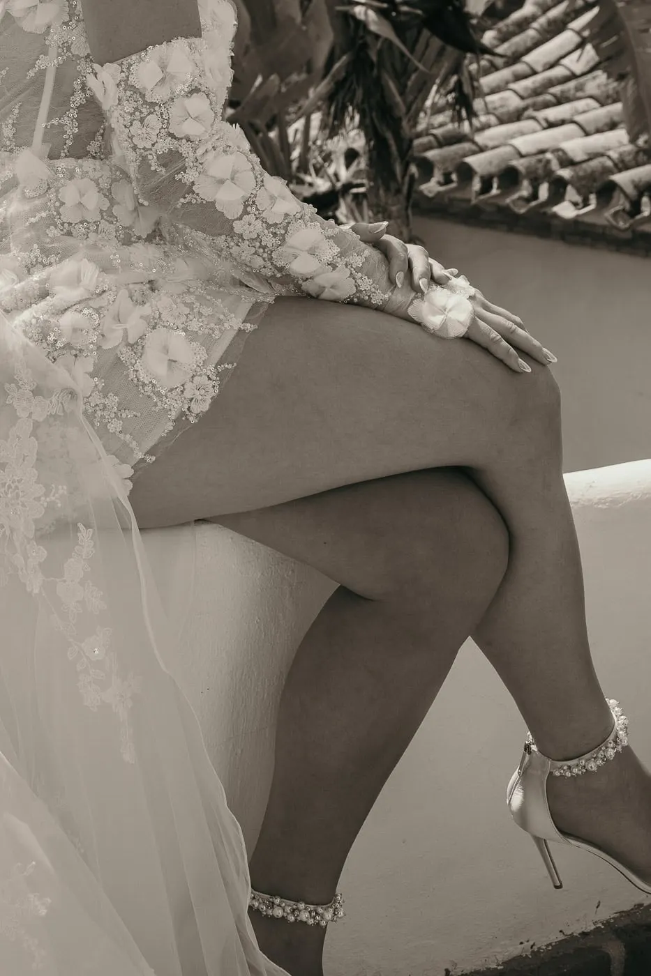 Sepia detail of the bride's crossed legs, lace sleeve and pearl ankle strap on a ledge, Hacienda San José, Mijas