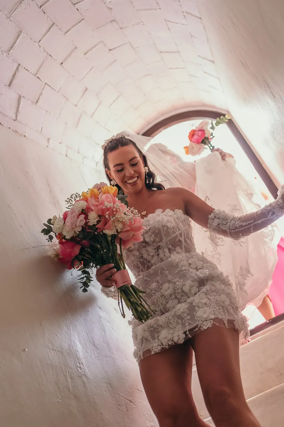 Bride with her bouquet smiling as she walks down a white staircase under an arched window, Hacienda San José, Mijas