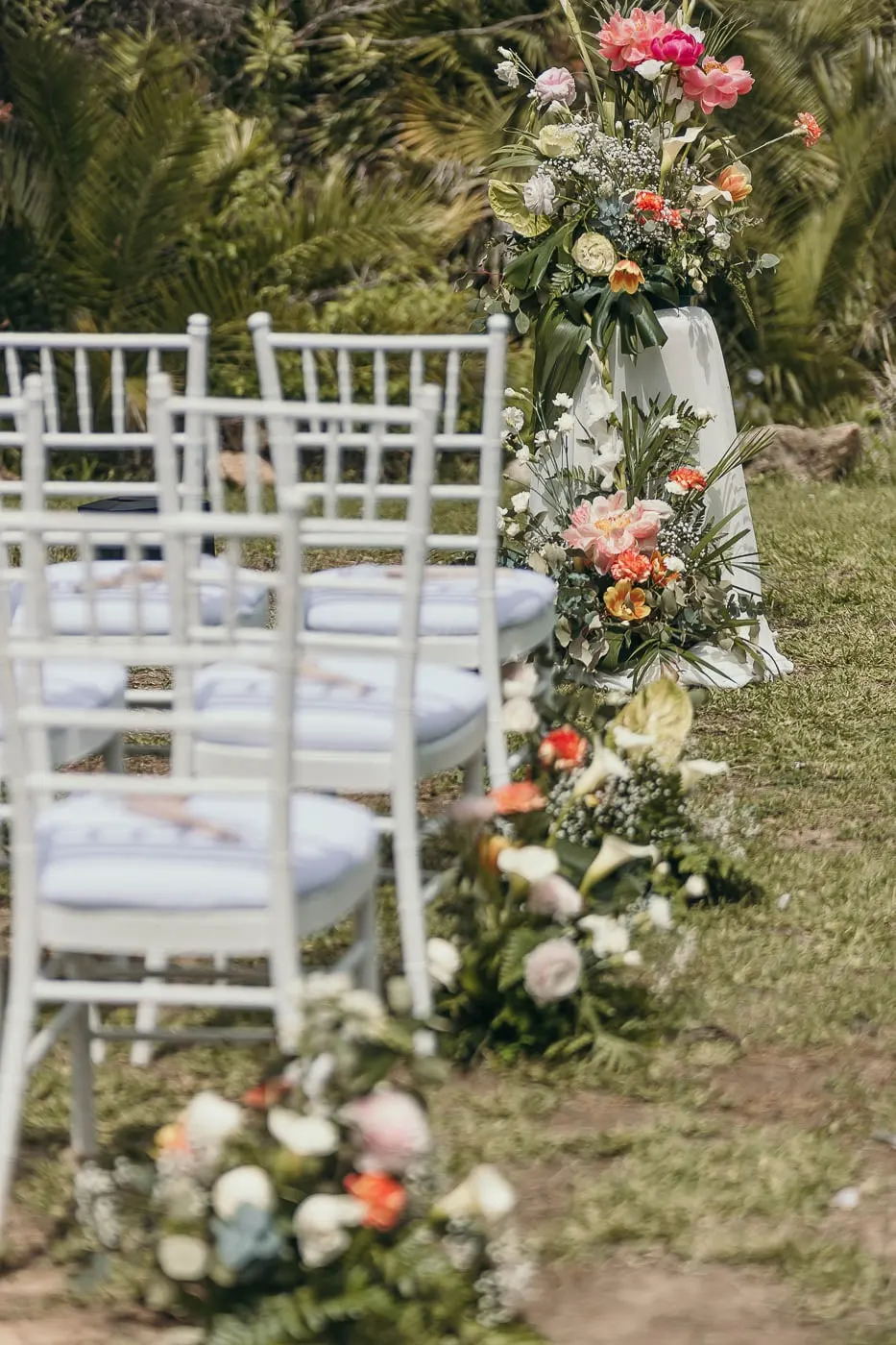Ceremony aisle lined with white chairs and arrangements of pink and coral flowers, Hacienda San José, Mijas