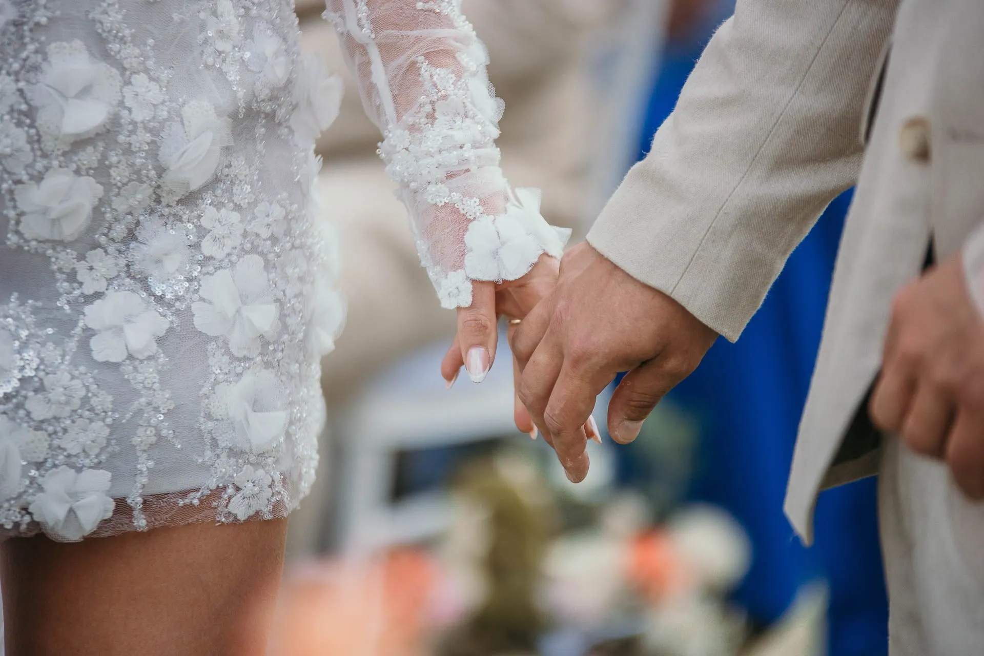 Close-up of the bride and groom holding hands, her lace sleeve and floral dress in focus, Hacienda San José, Mijas