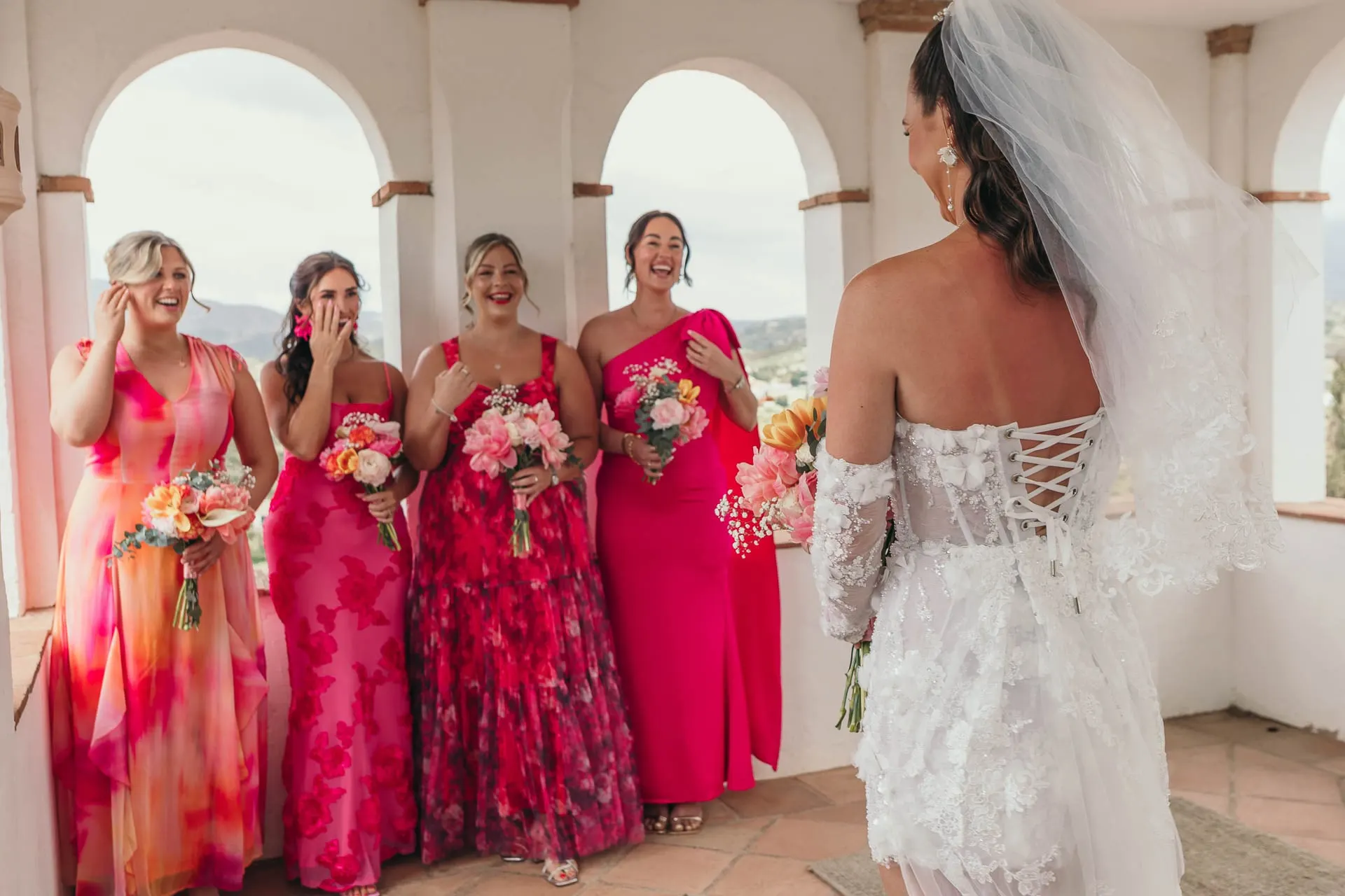 Bridesmaids in pink react with joy as they see the bride in her dress for the first time, Hacienda San José, Mijas