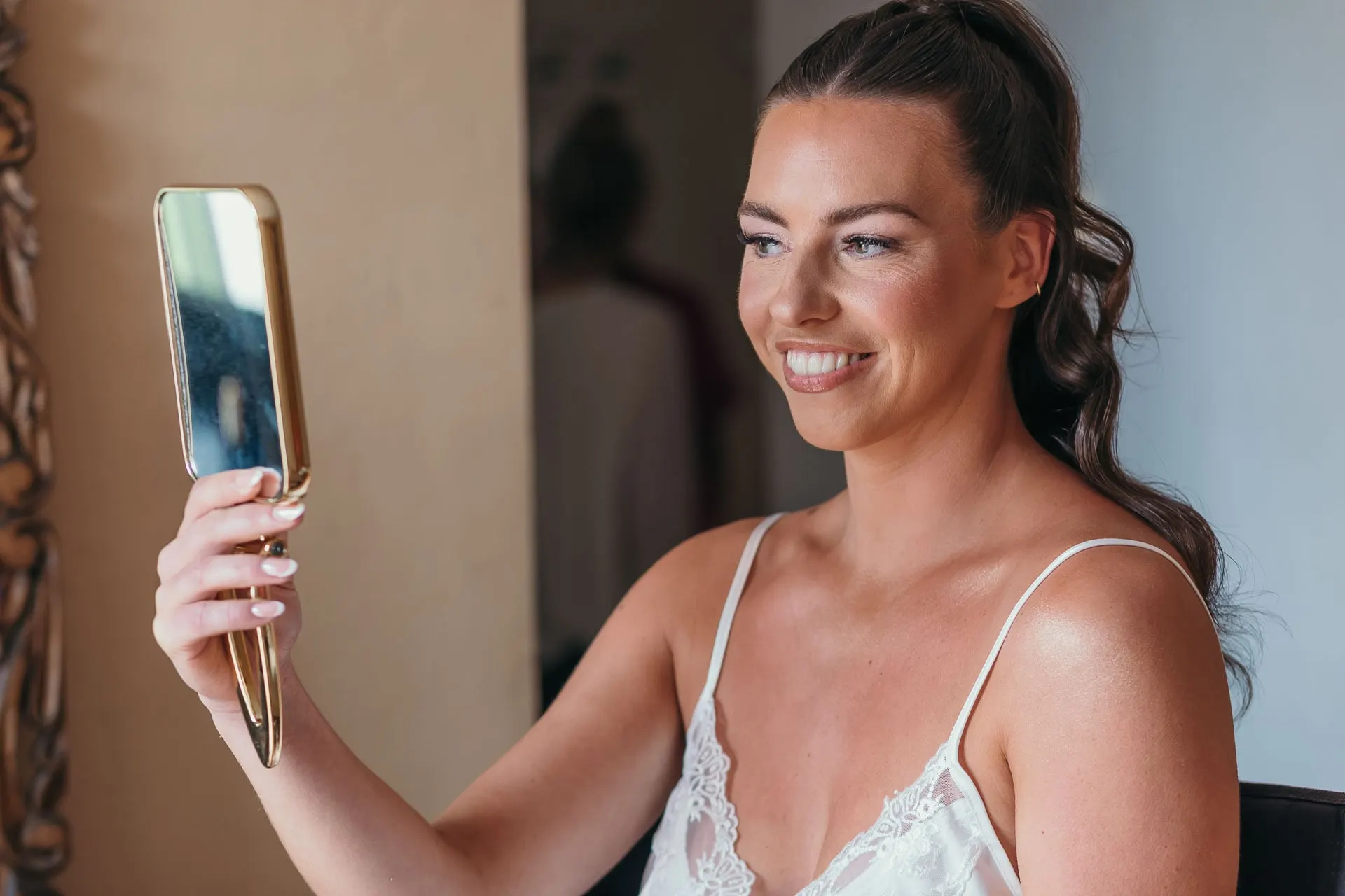 Bride smiling at her reflection in a gold hand mirror before getting dressed, Hacienda San José, Mijas