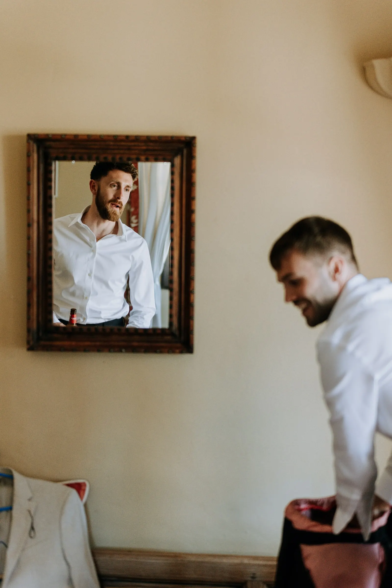 Groom getting dressed, reflected in a framed mirror at Hacienda San José