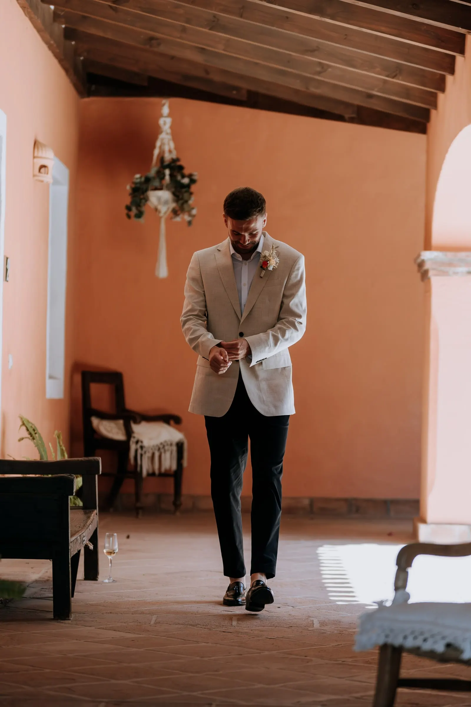 Groom walking through a terracotta-walled room with a wooden ceiling at Hacienda San José