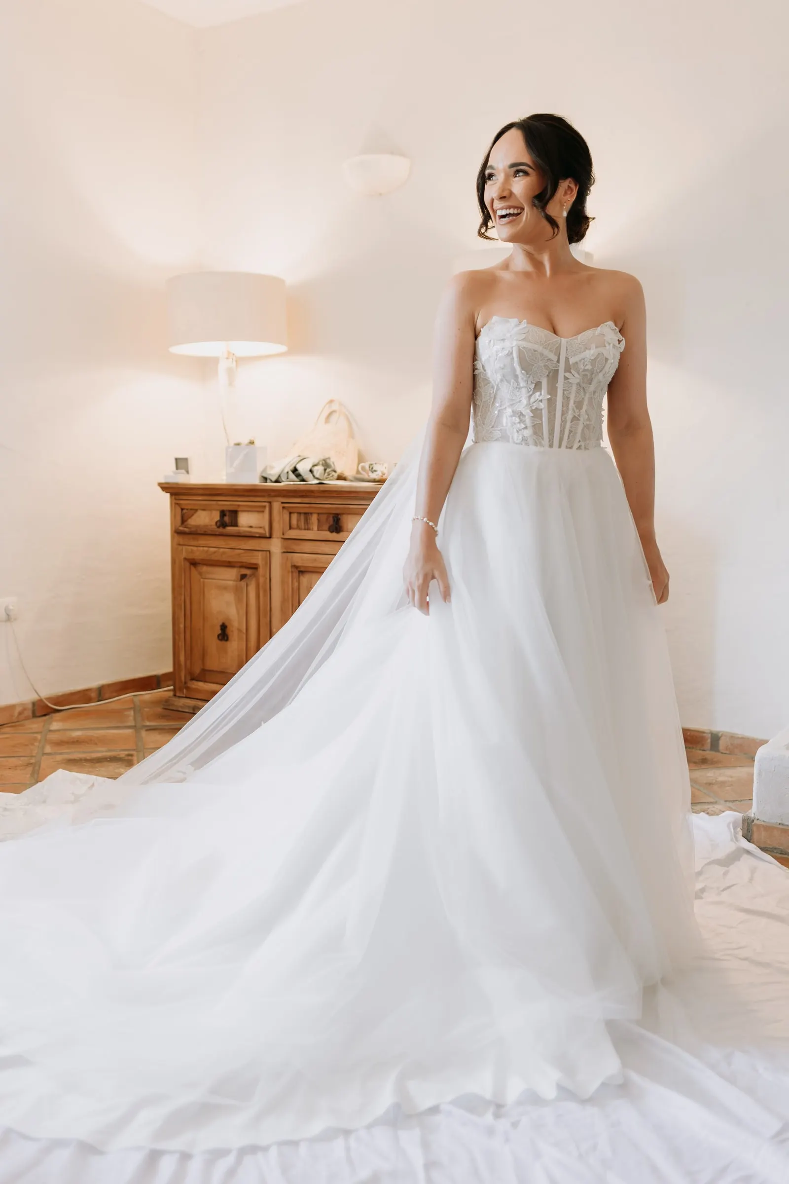 Bride in her corset gown and long veil smiling in the bridal suite, Mijas