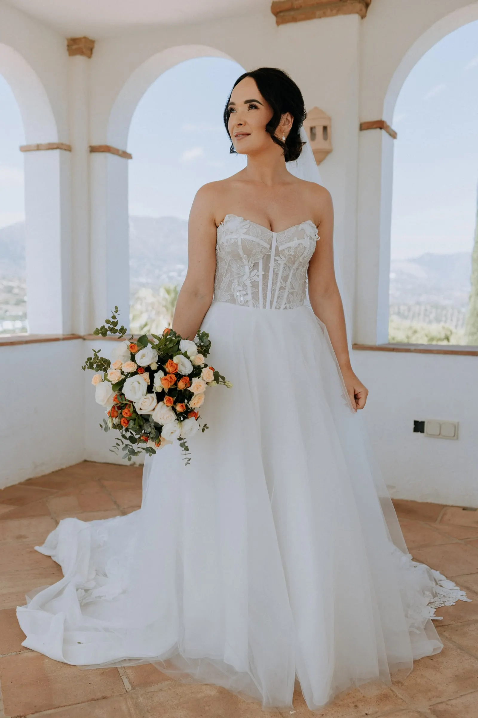 Bride with a bouquet of white and orange roses in the white arched tower of Hacienda San José, Mijas
