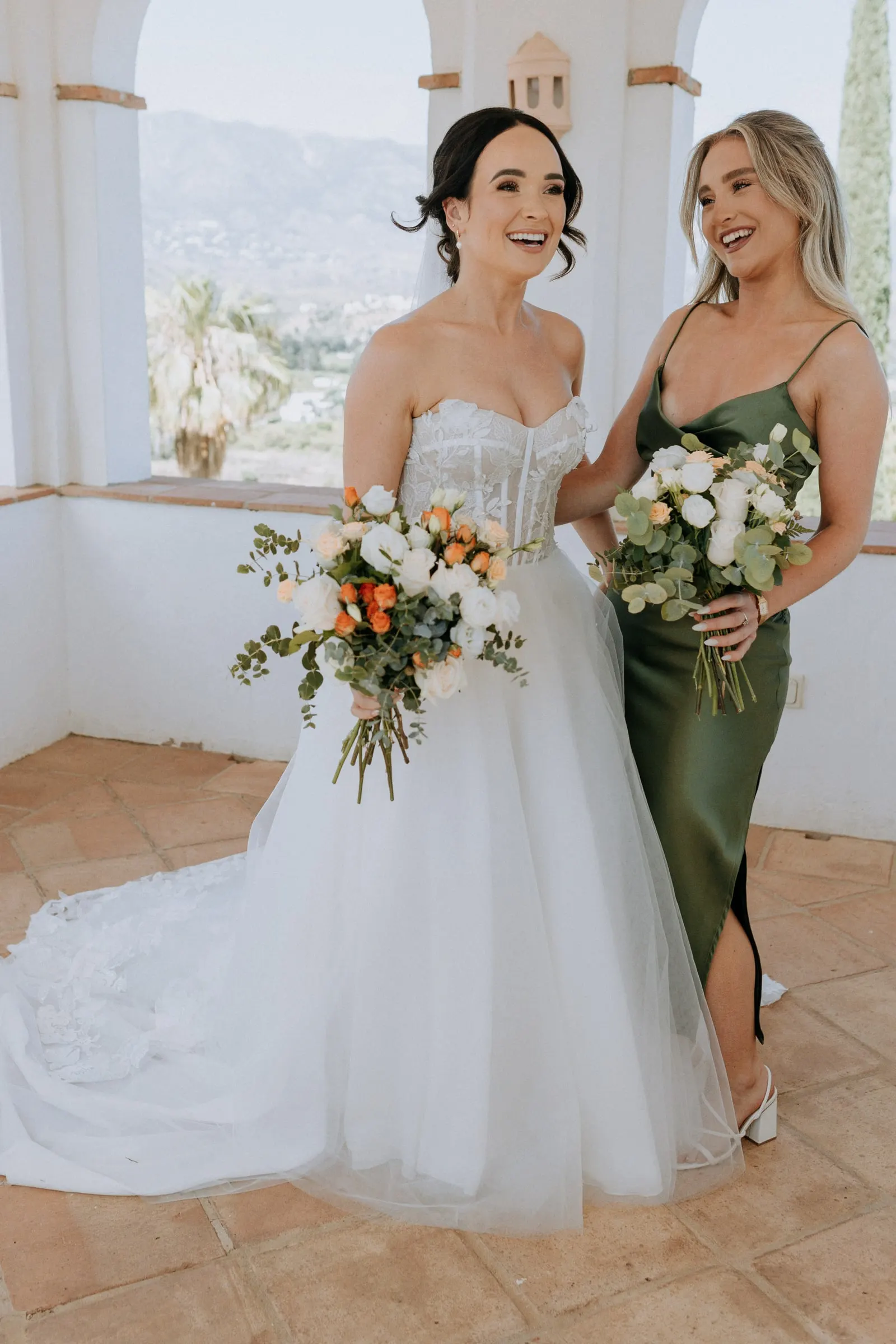 Bride laughing with a bridesmaid in olive satin inside the tower, Mijas