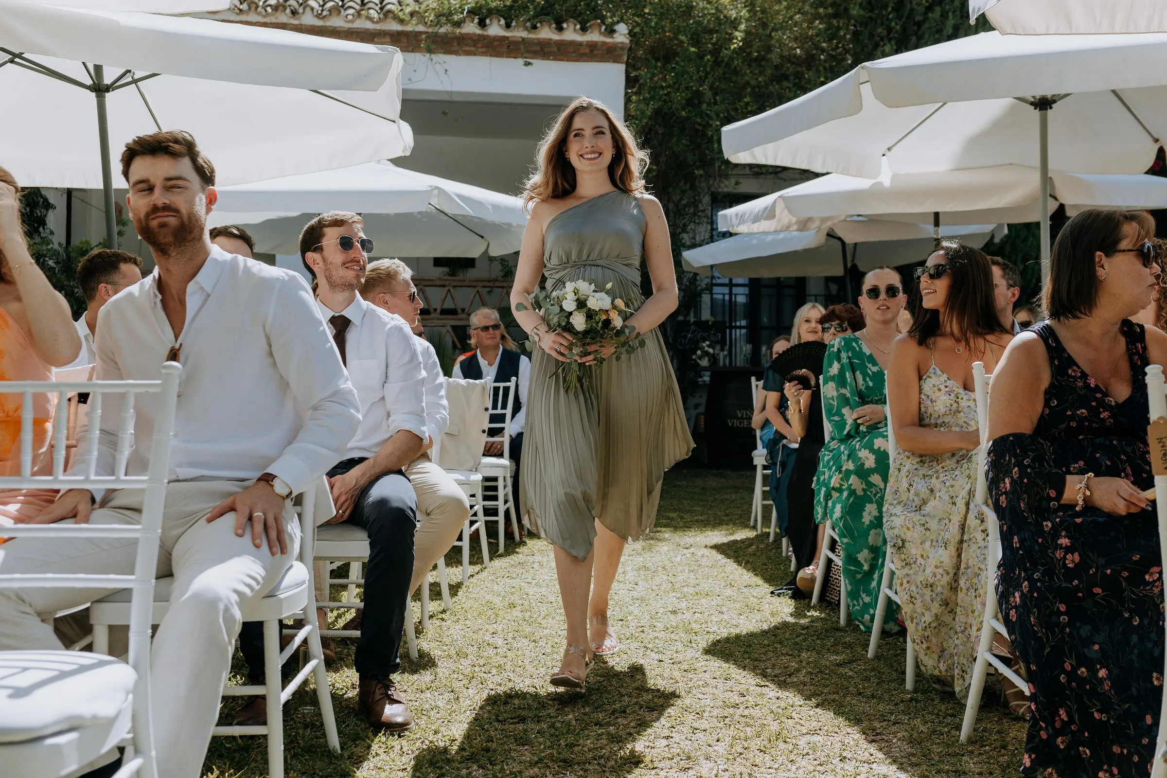 Bridesmaid walking down the aisle between white parasols at the garden ceremony, Mijas