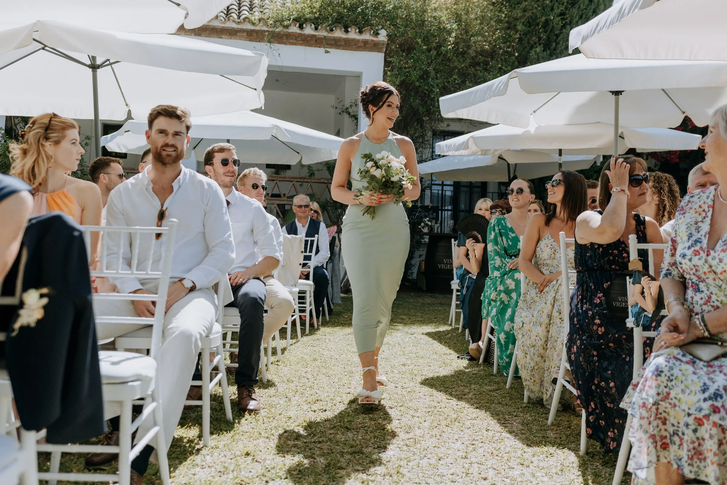 Last bridesmaid walking down the aisle under the parasols at Hacienda San José