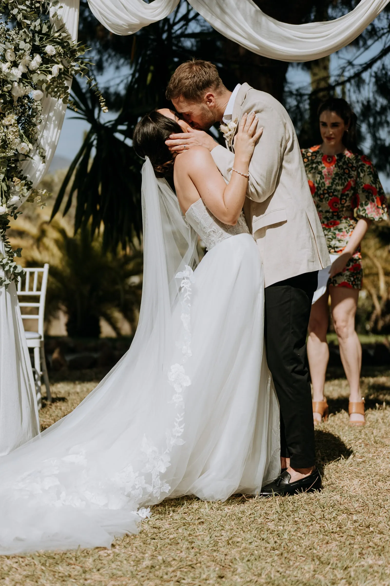 First kiss under the arch of white drapes and flowers, Mijas