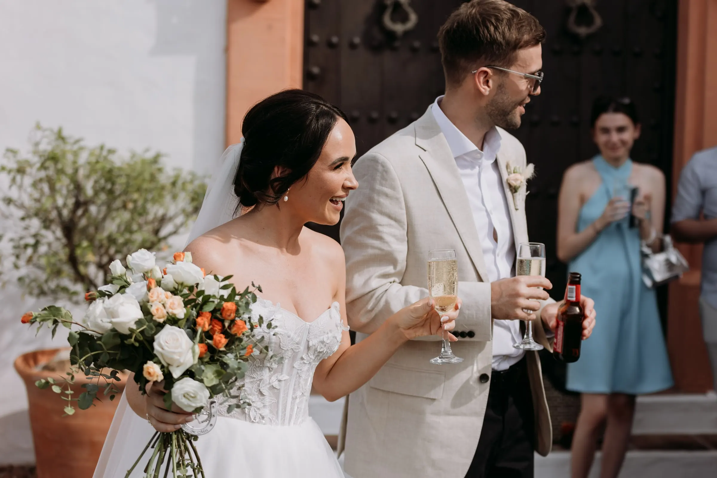 Bride and groom with glasses of cava by the old wooden door of the hacienda, Mijas