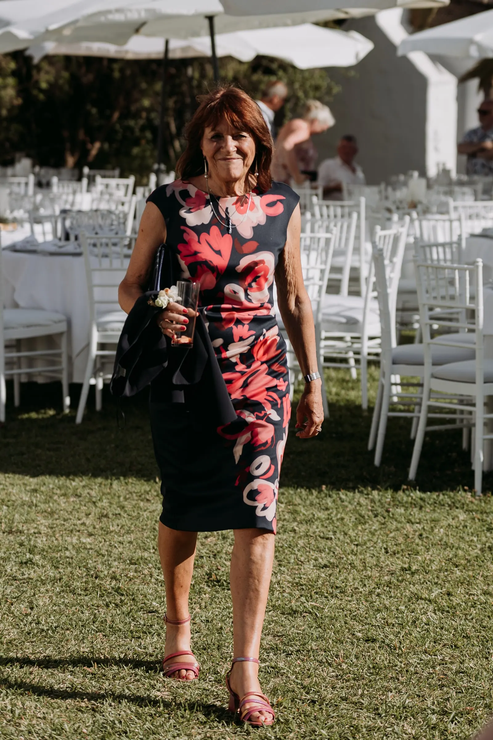 Guest in a floral dress walking across the lawn past the dinner tables, Mijas