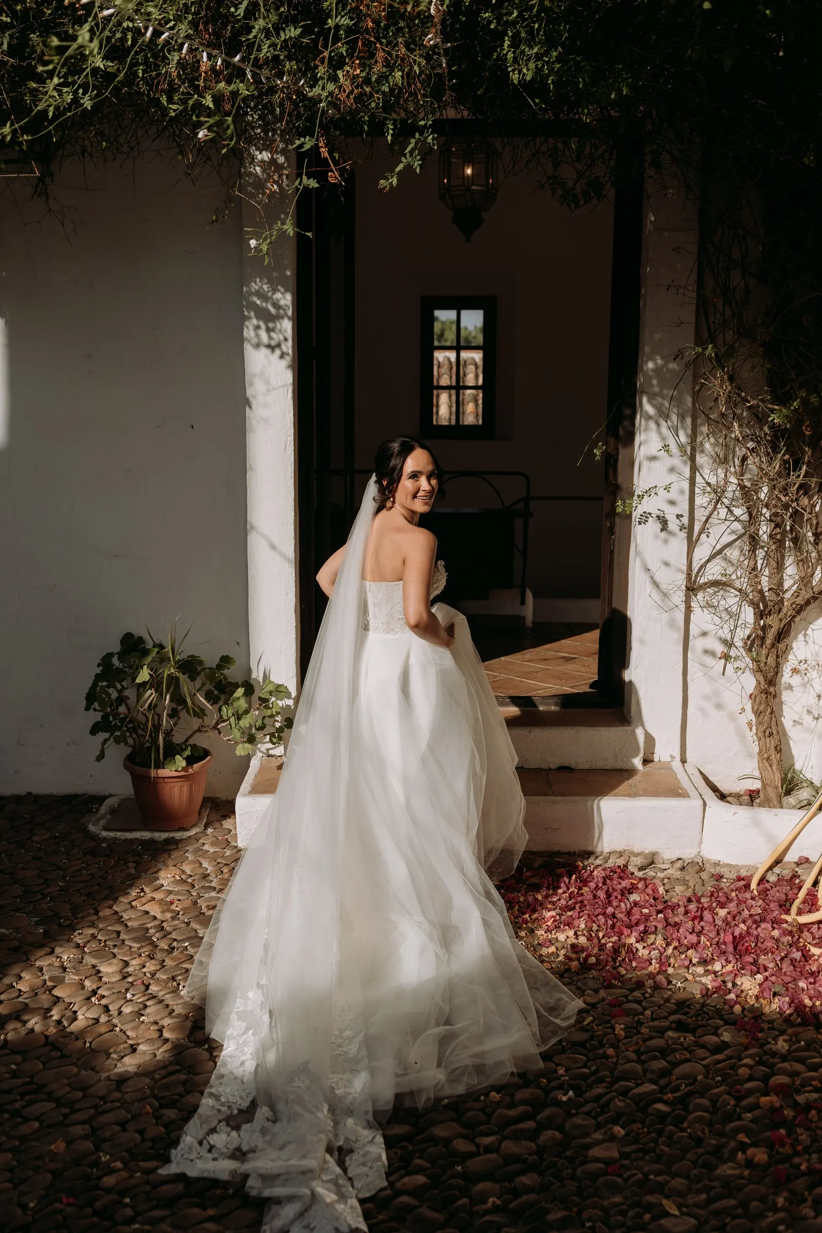 Bride looking back in a whitewashed doorway with her long veil on the cobbles, Hacienda San José